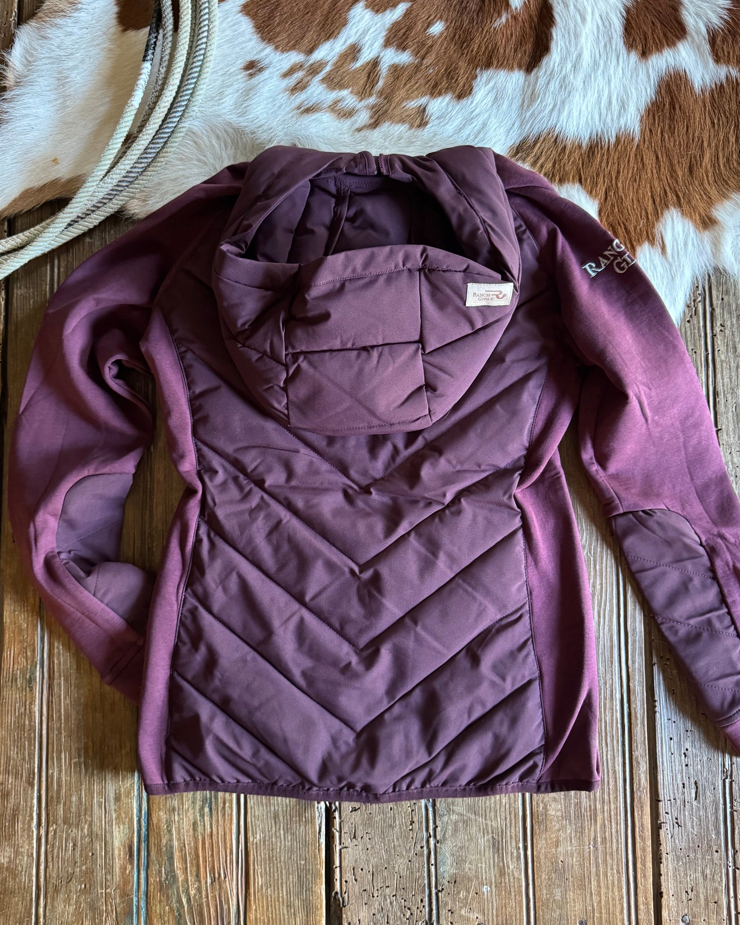 Purple quilted jacket on a wooden surface with a cowhide rug and lasso.