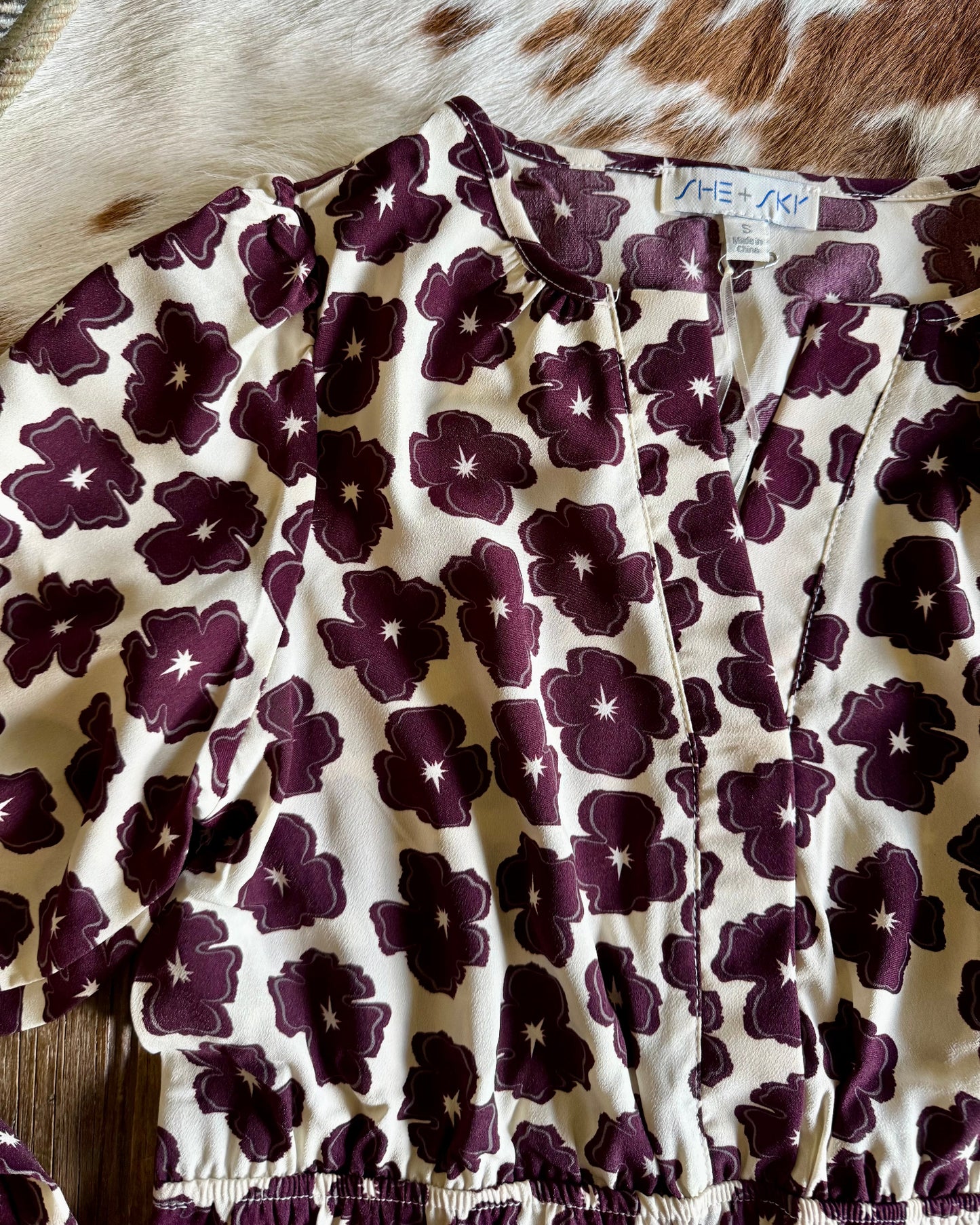 Floral patterned fabric with purple flowers on a white background, laid over a cowhide rug.