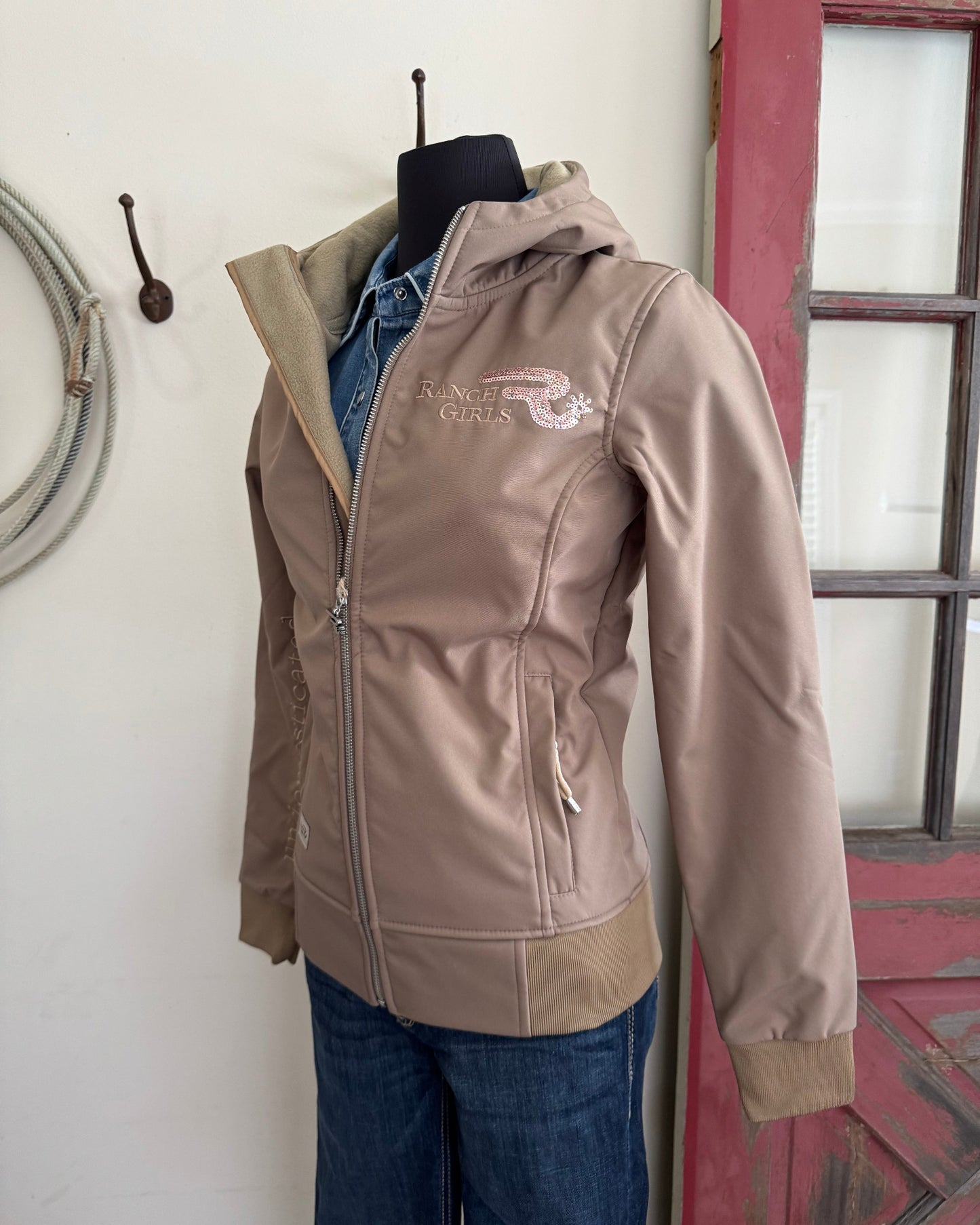 Brown jacket with a logo worn by a person, leaning against a wall.
