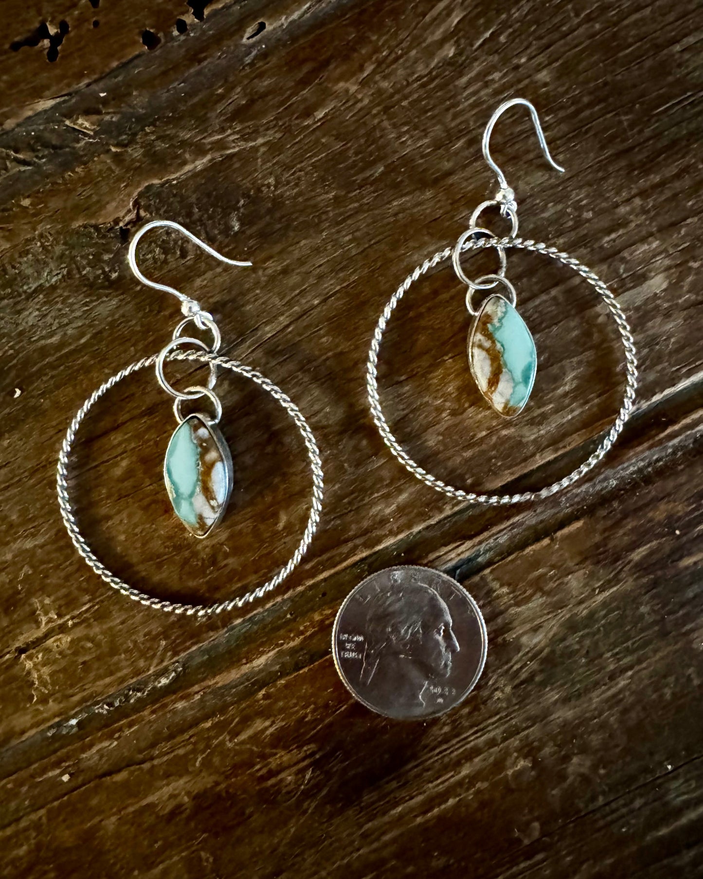 Silver hoop earrings with turquoise stones on a wooden surface, next to a penny for scale.