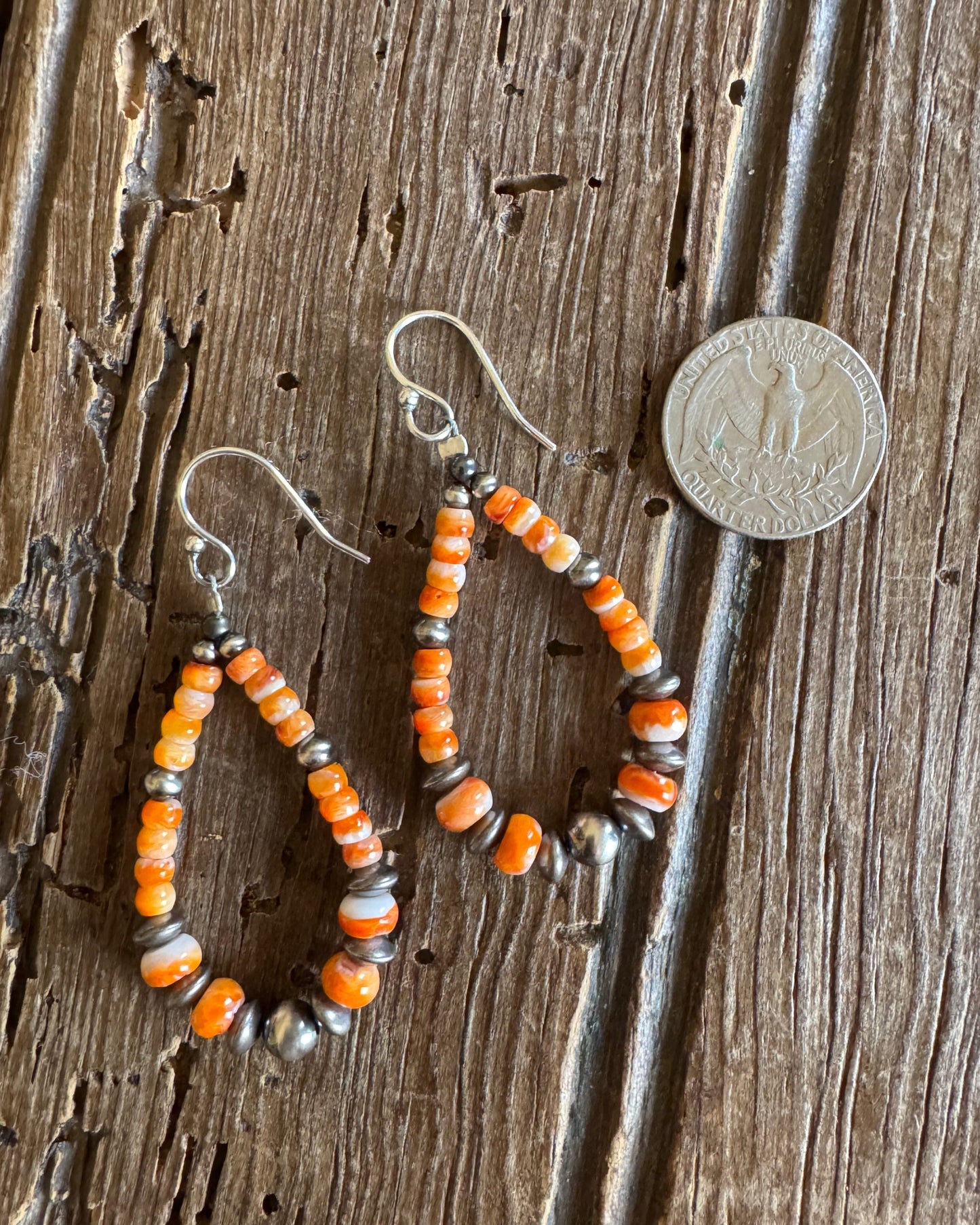 Orange spiny loop earrings with sterling silver pearls on rustic wood background with quarter