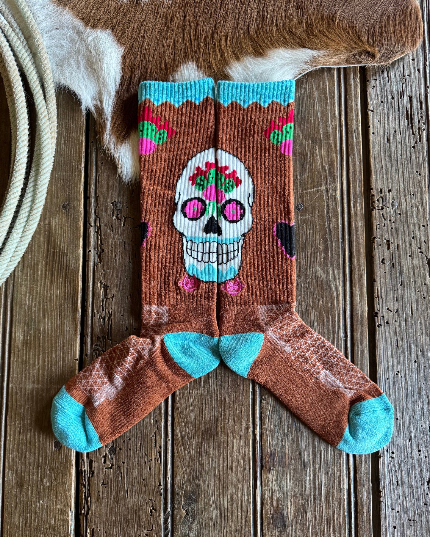 Colorful skull design sock on a wooden surface with cowhide rug and lasso.