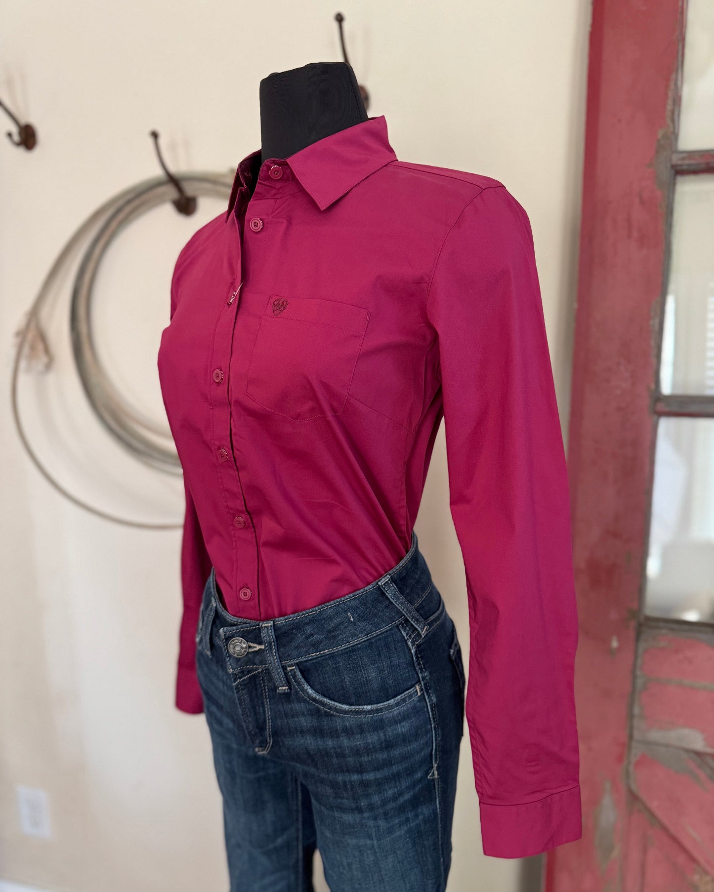 Pink shirt on a mannequin with jeans against a neutral wall.