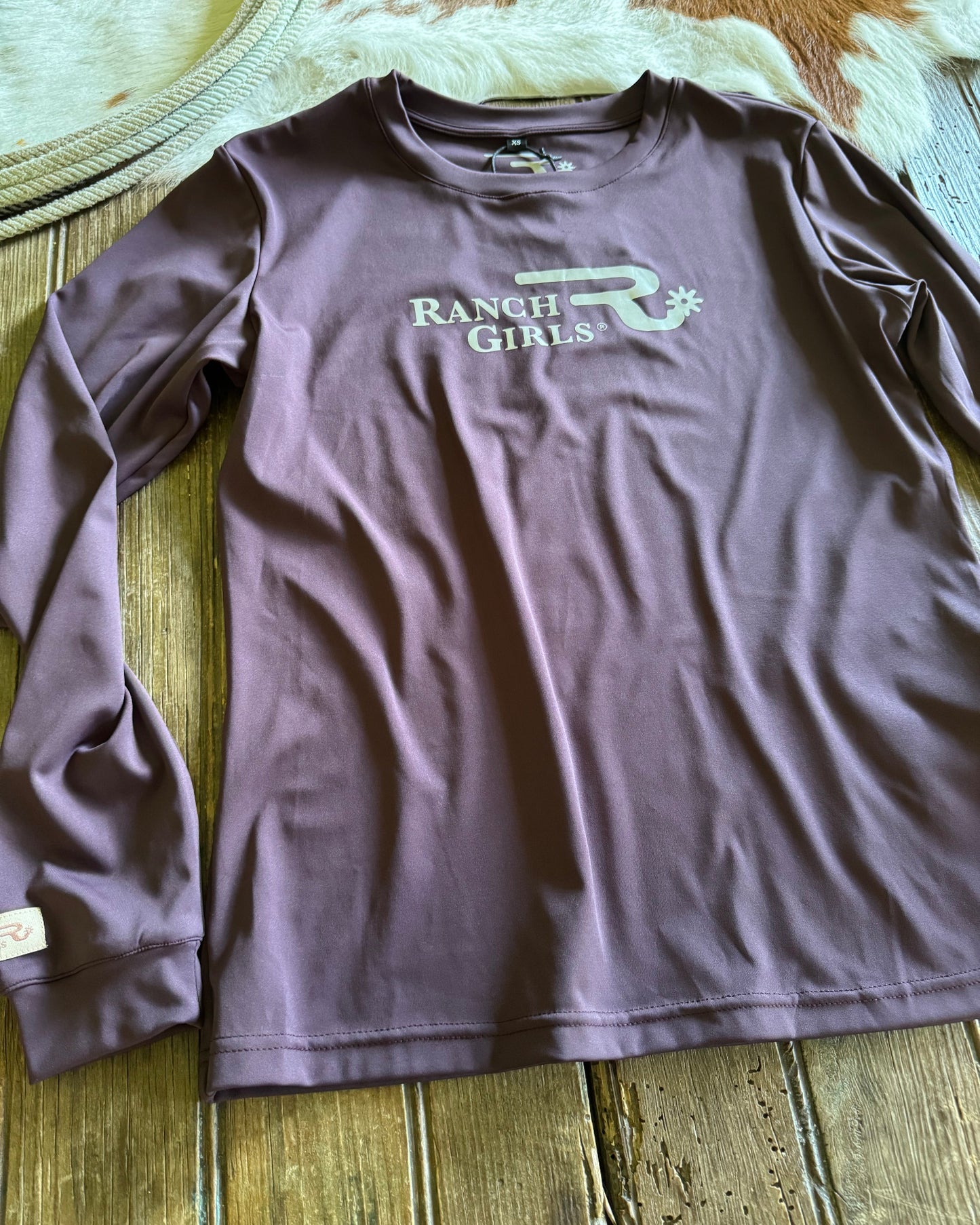 Purple t-shirt with 'Ranch Girls' logo on a wooden surface