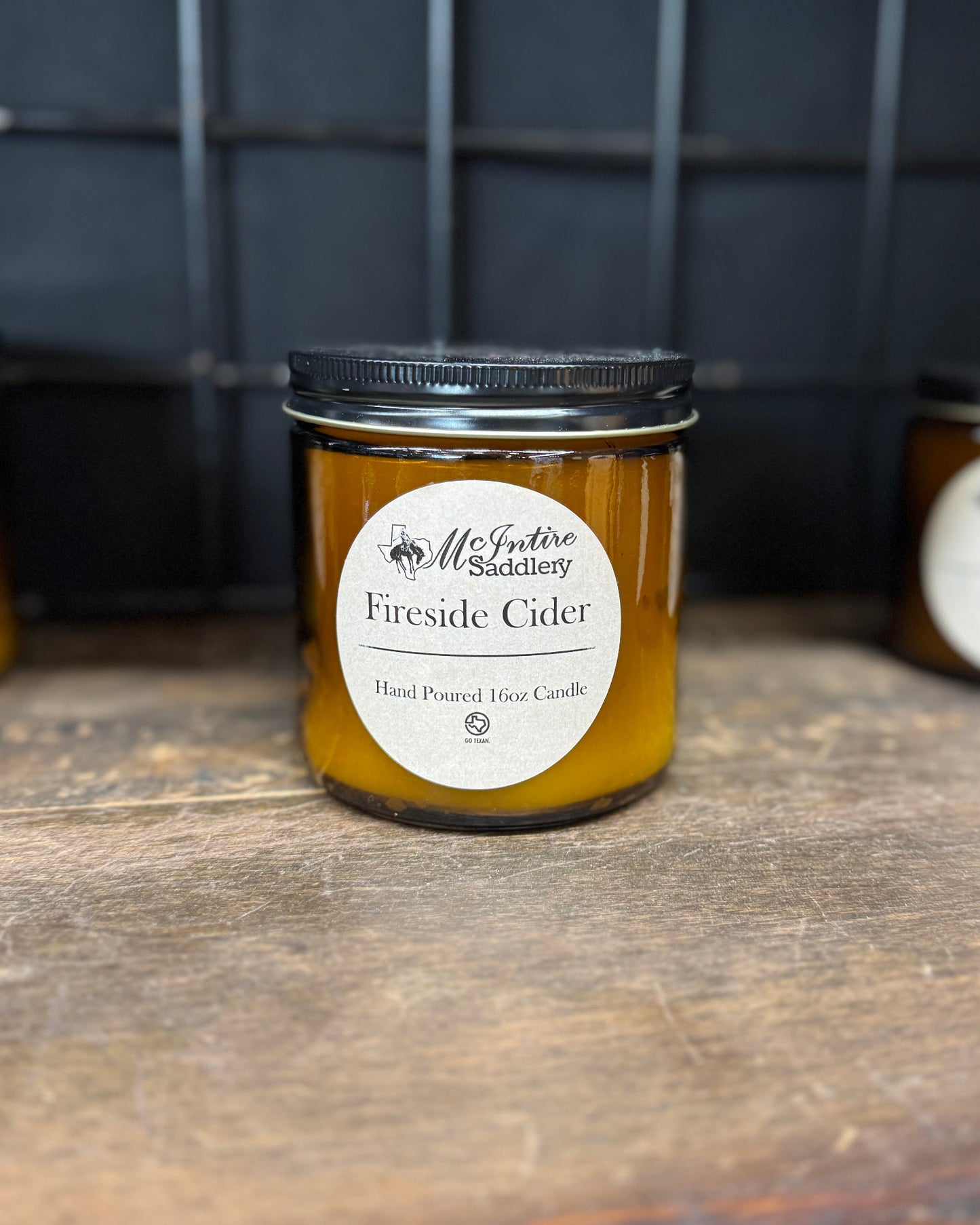 Jar of 'Fireside Cider' candle on a wooden surface with a metal grid background