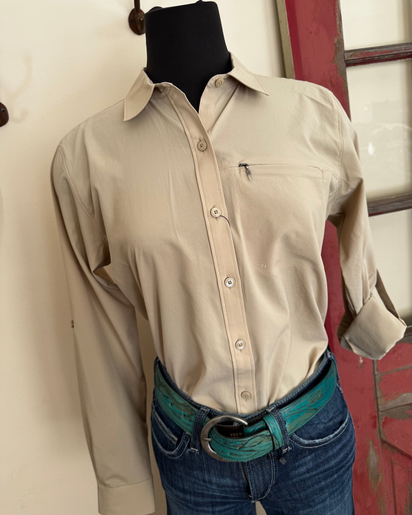 Person wearing a beige shirt and blue jeans with a belt, standing on a white floor.