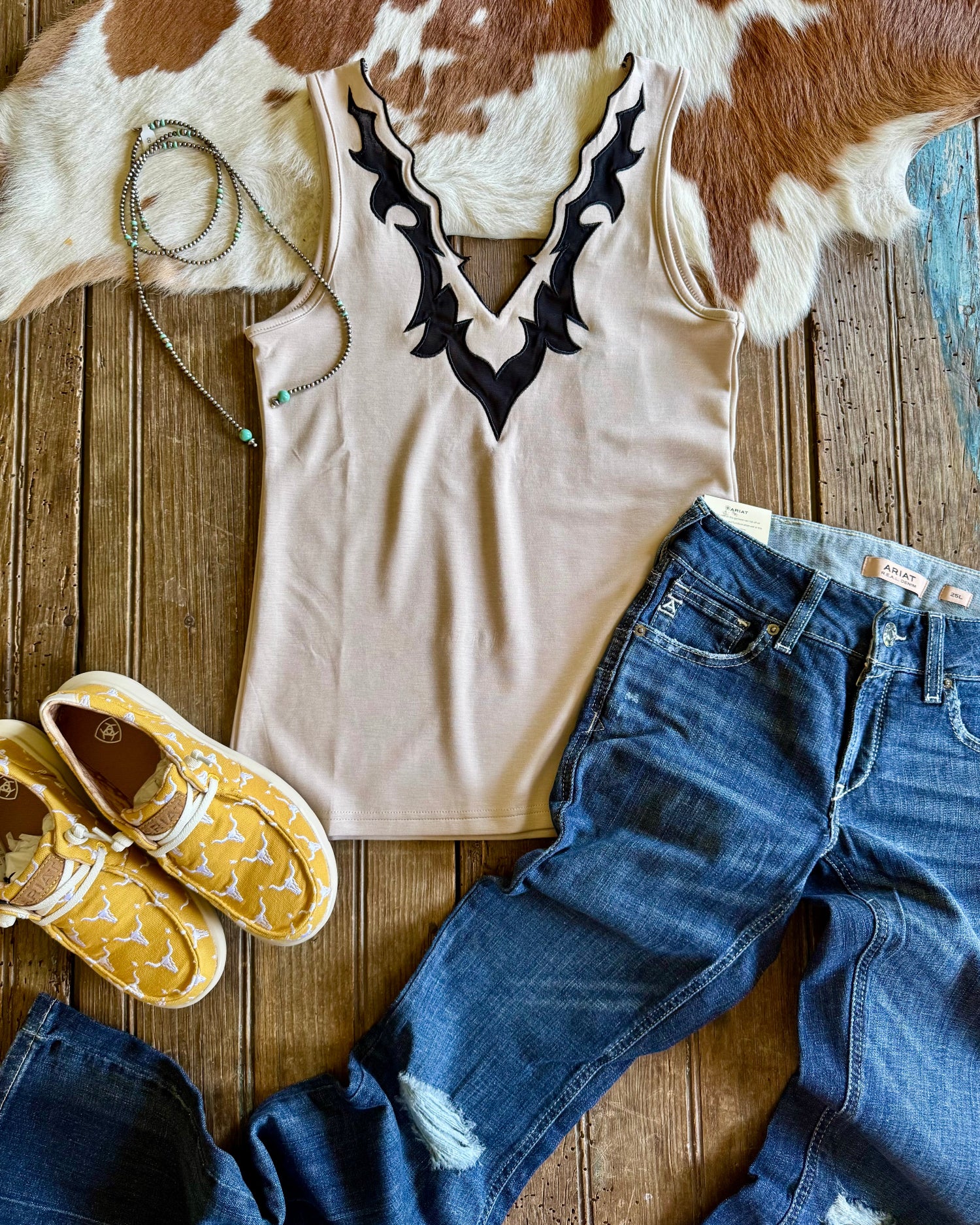 Llano Tank top flat lay with jeans, shoes and silver pearl necklace on rustic wood and cowhide background