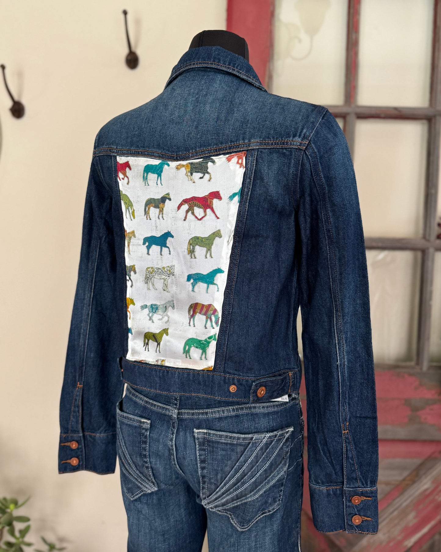 Denim jacket with horse pattern on the back, displayed against a neutral wall.