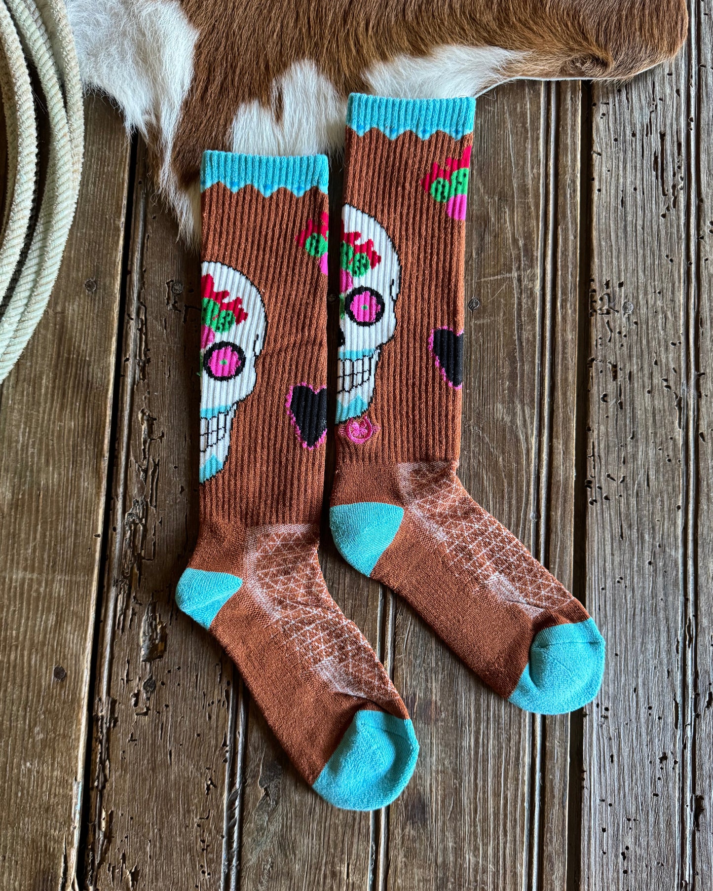 Pair of brown socks with colorful designs and blue toes on a wooden surface.