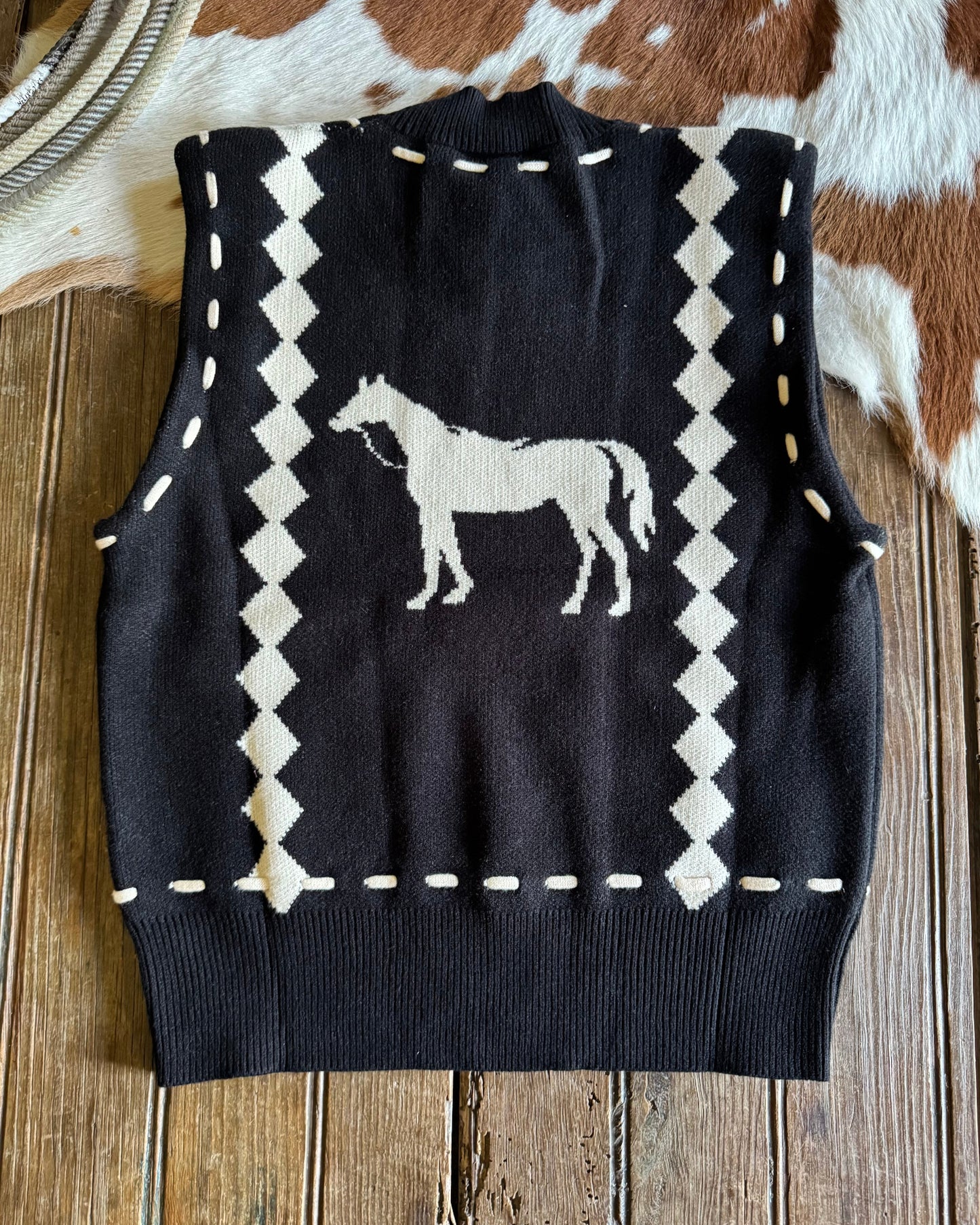 Black sweater vest with white horse design on a wooden surface
