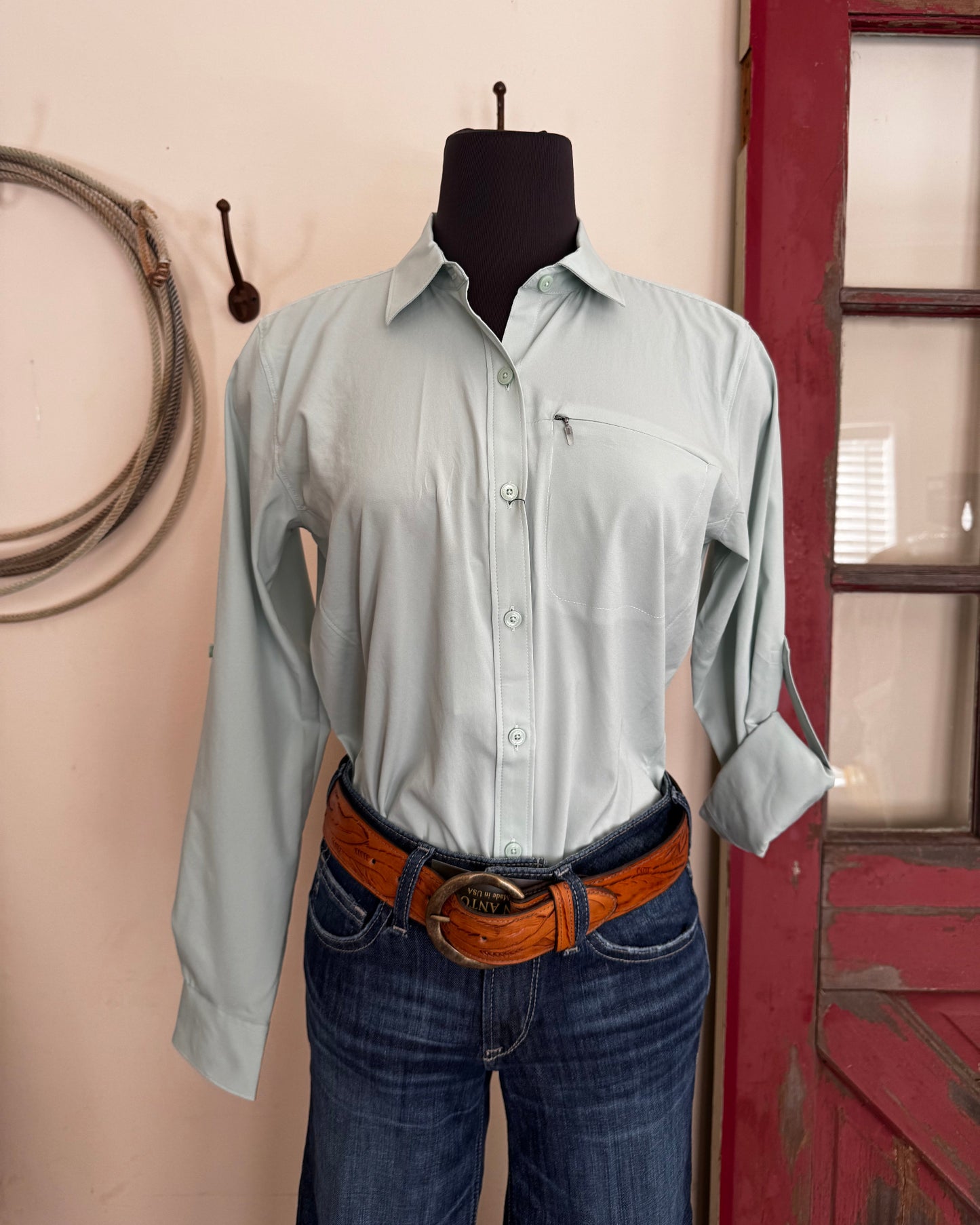 Person wearing a light green shirt and blue jeans with a brown belt, standing in front of a red vehicle.