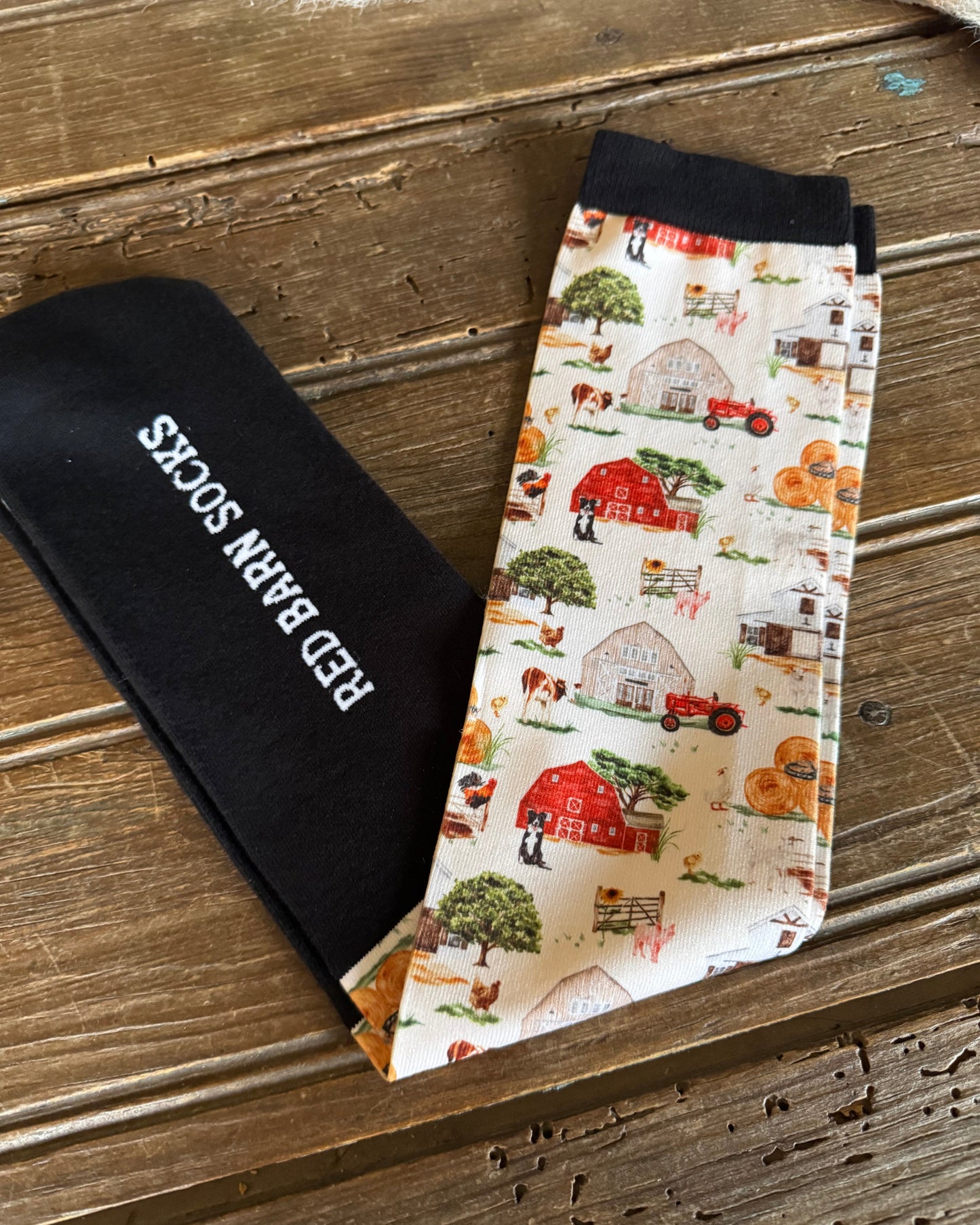 Pair of socks with farm-themed pattern and 'Red Barn Socks' label on a wooden surface