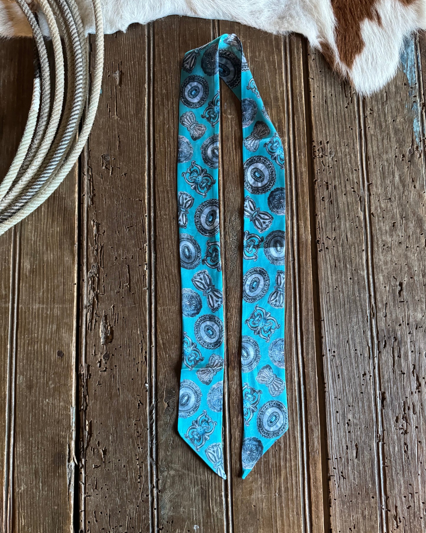Blue patterned ribbon scarf on a wooden surface with cowhide leather and rope.