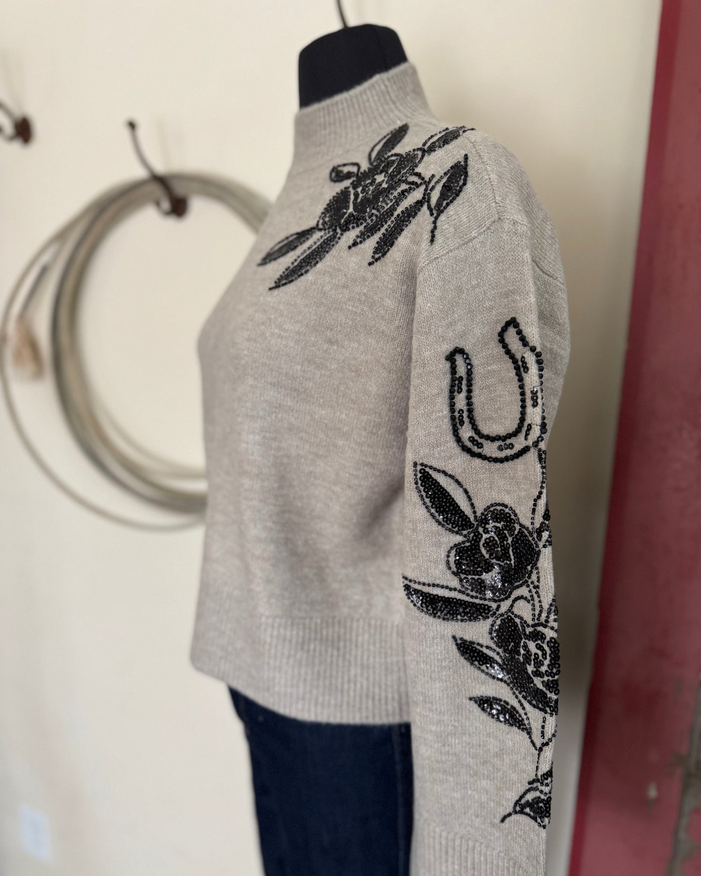 Gray sweater with black floral and horseshoe designs on a mannequin against a neutral background.