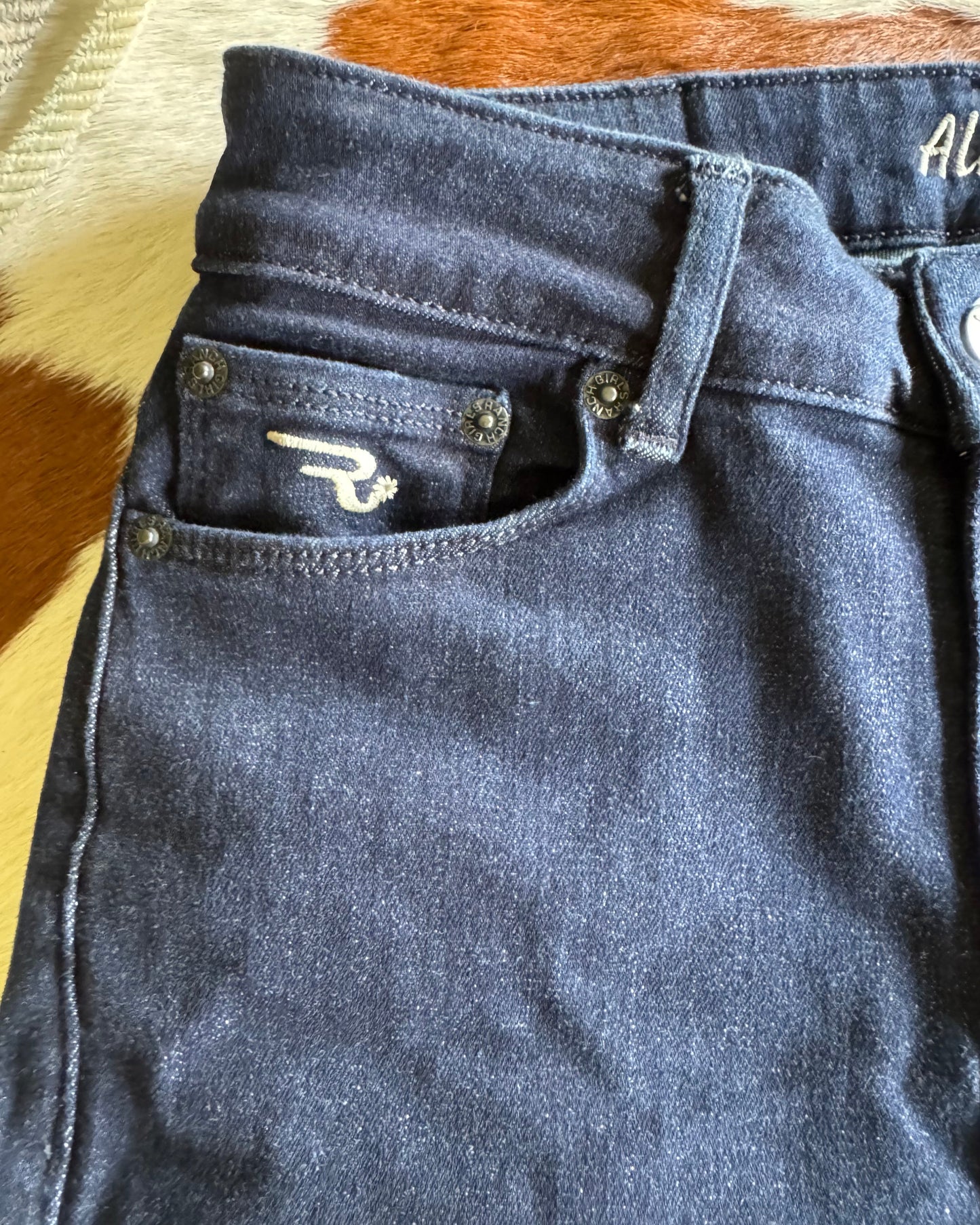 Close-up of a dark denim jacket with a brand logo on a multicolored fabric background