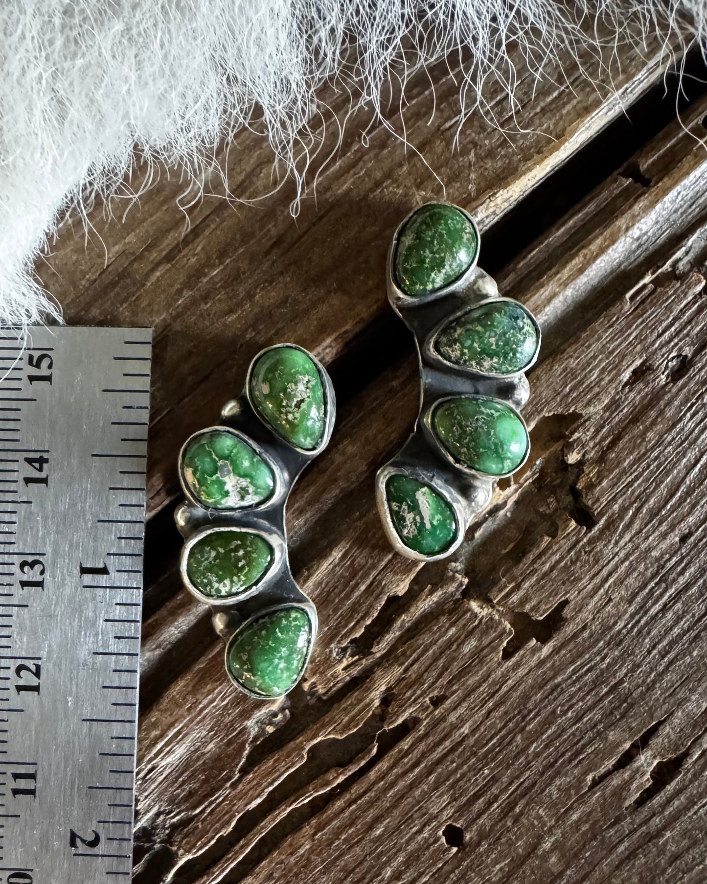 Two silver earrings with green gemstones on a wooden surface with a ruler for scale.