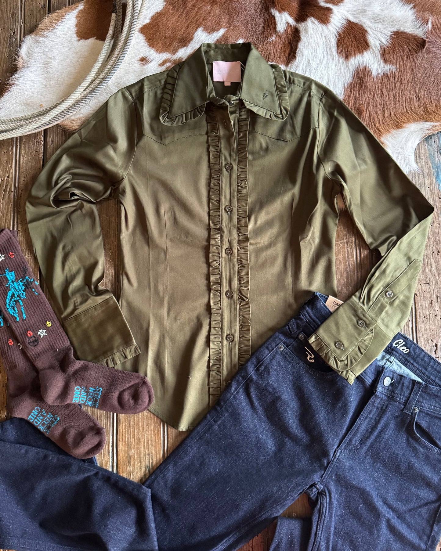 Frill Blouse, blue jeans, and brown socks on a wooden surface with a cowhide rug.