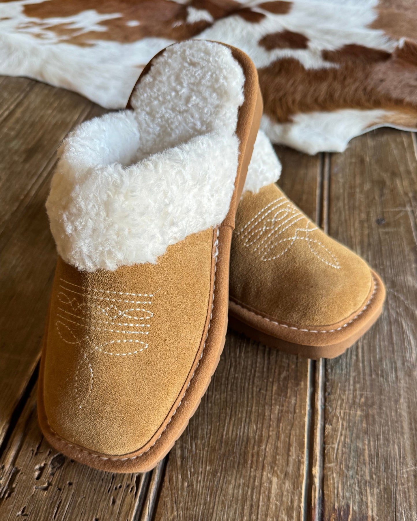 Brown slippers with white fur lining on a wooden surface