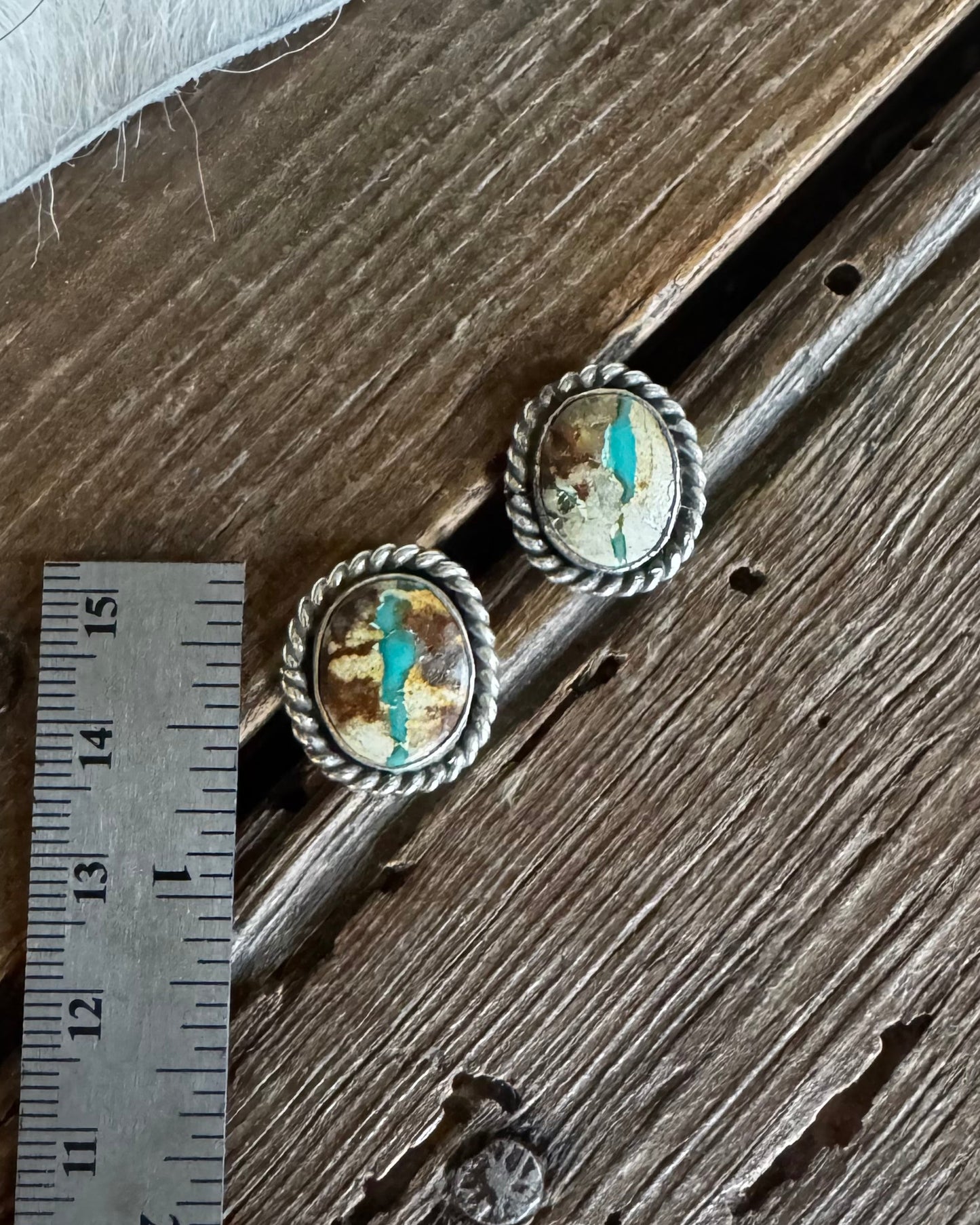 Pair of earrings on a wooden surface with a ruler for scale.