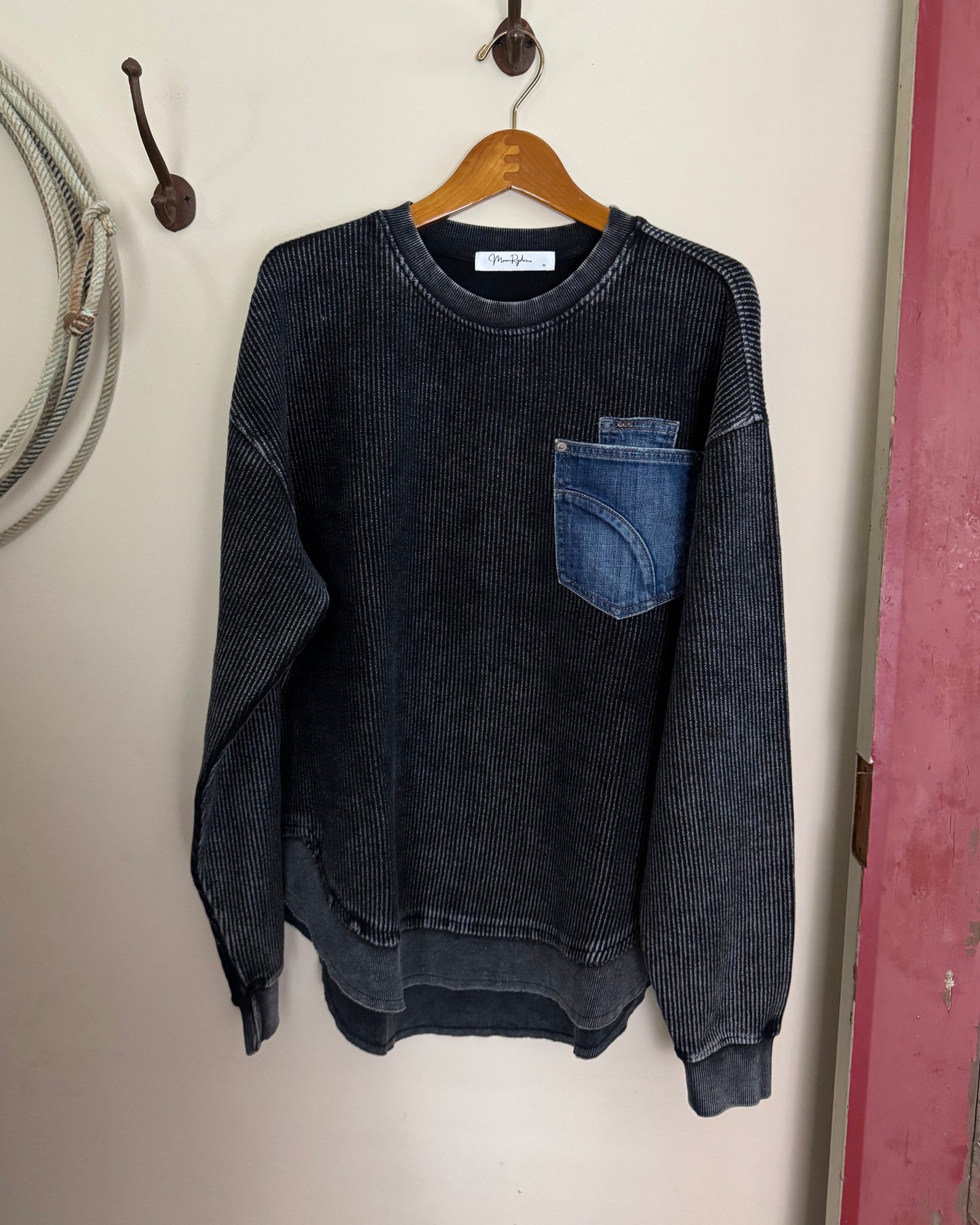 Dark long sleeved shirt on a white surface with a wooden hanger and metal object.