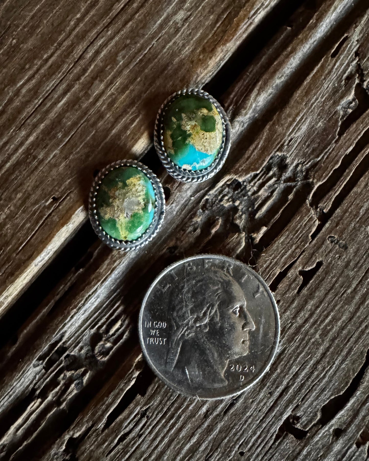 Two green stone earrings next to a quarter on a wooden surface