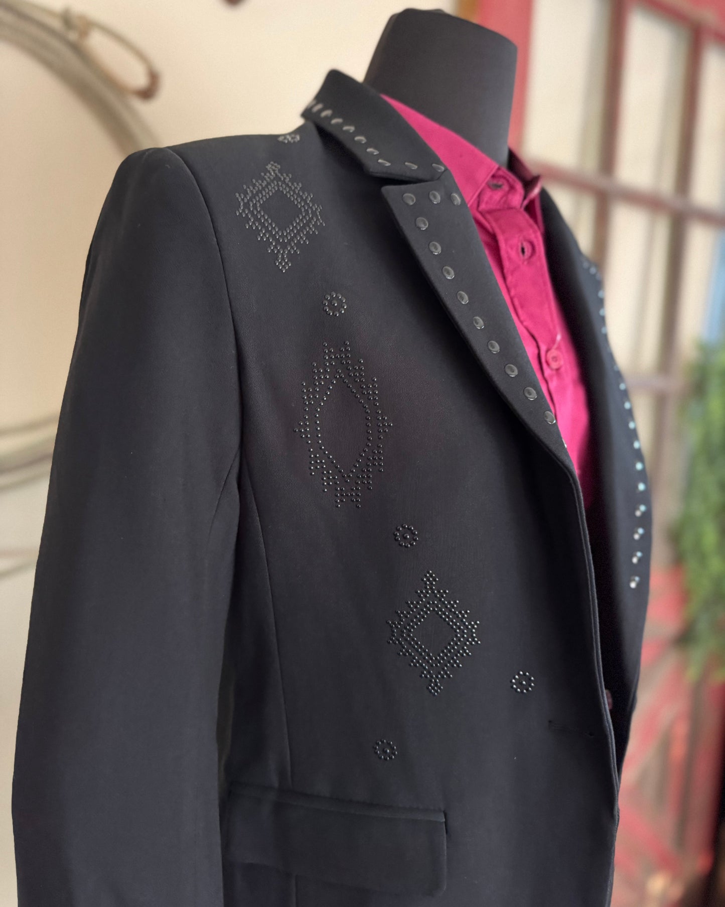 Black blazer with decorative patterns on a mannequin against a blurred background