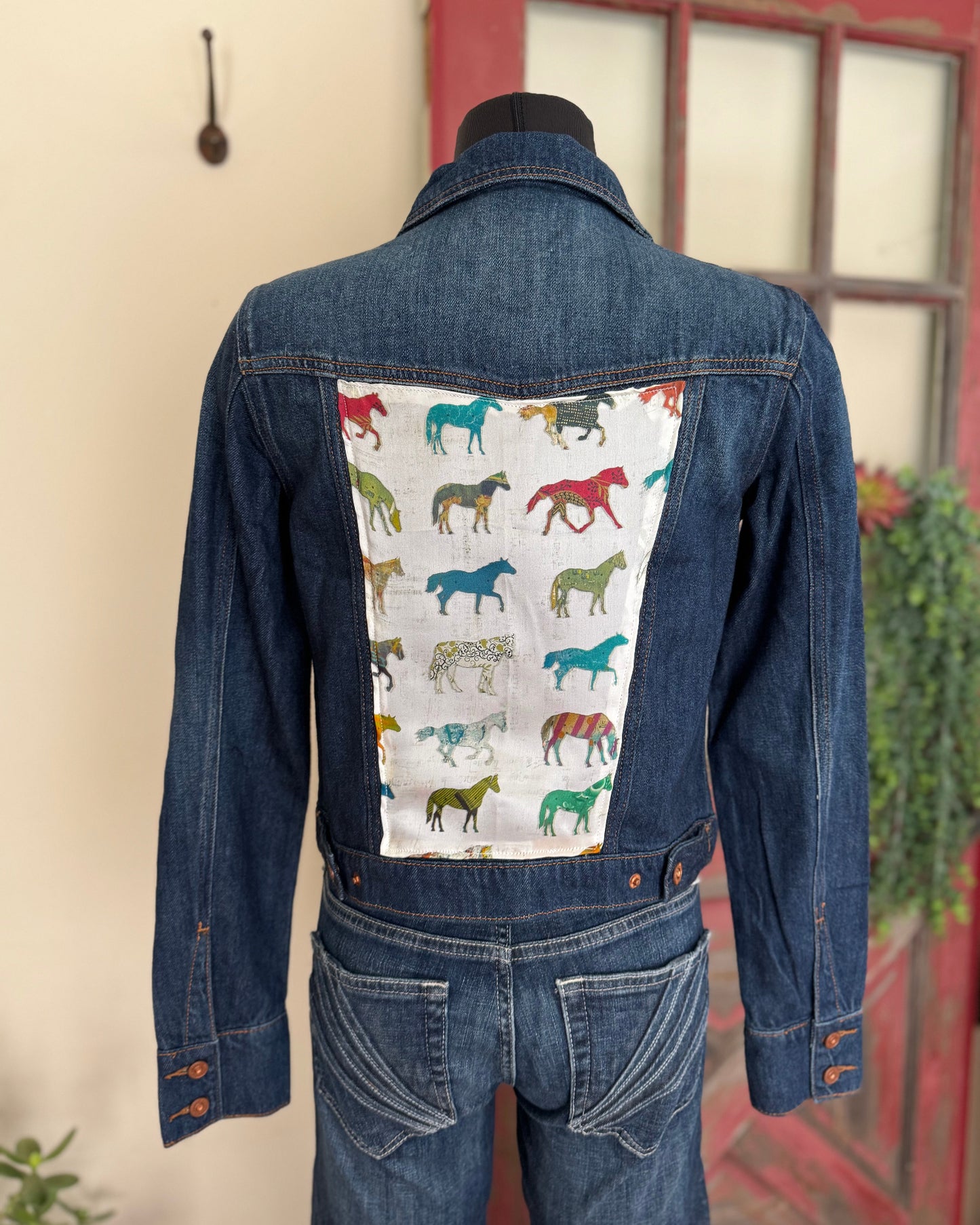 Denim jacket with horse pattern on the back, displayed against a neutral background.