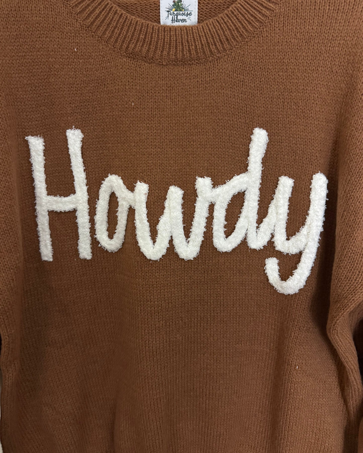 Brown sweater with white 'Howdy' text on a close-up view
