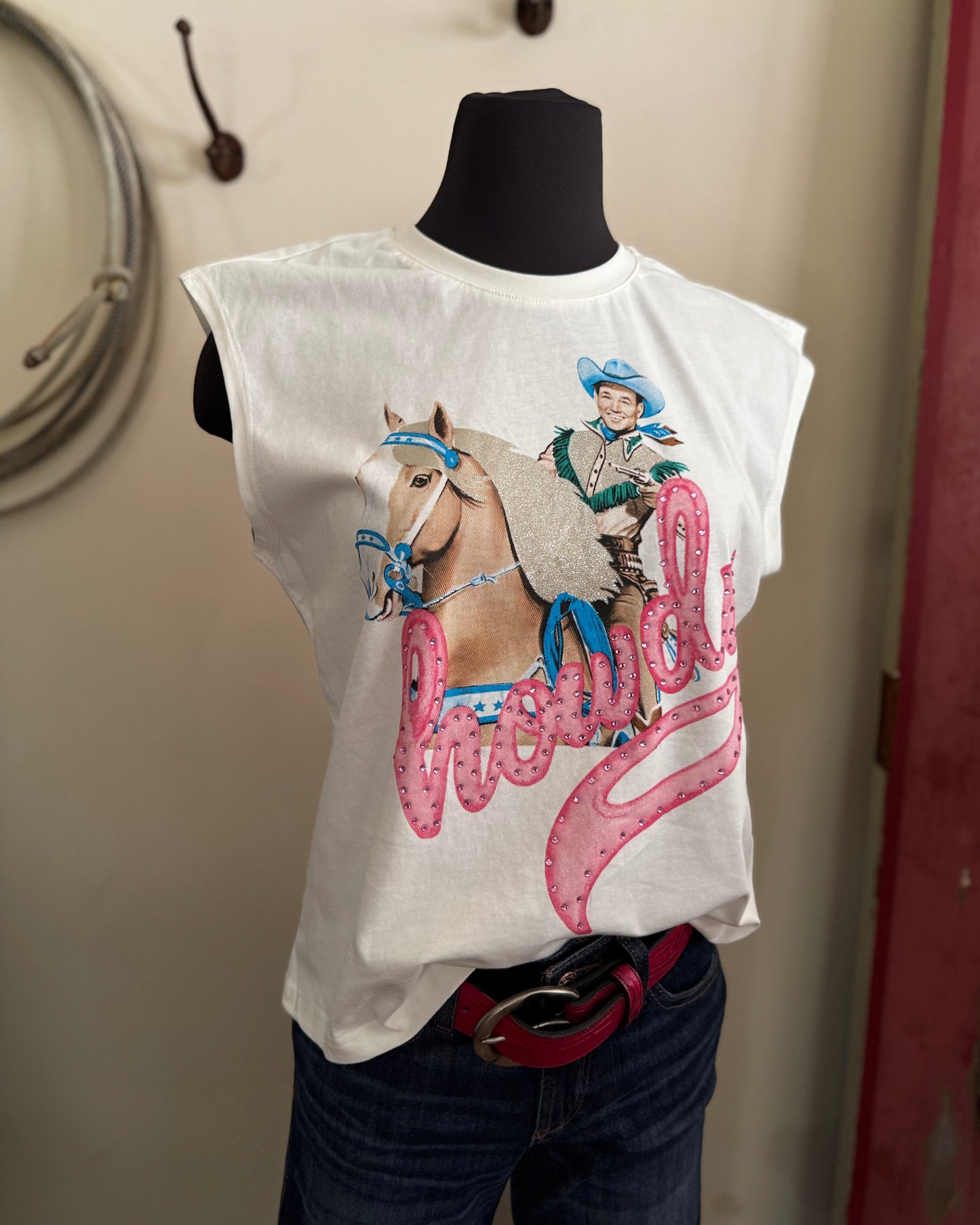 White t-shirt with a graphic of a cowboy and horse on a mannequin against a beige wall.