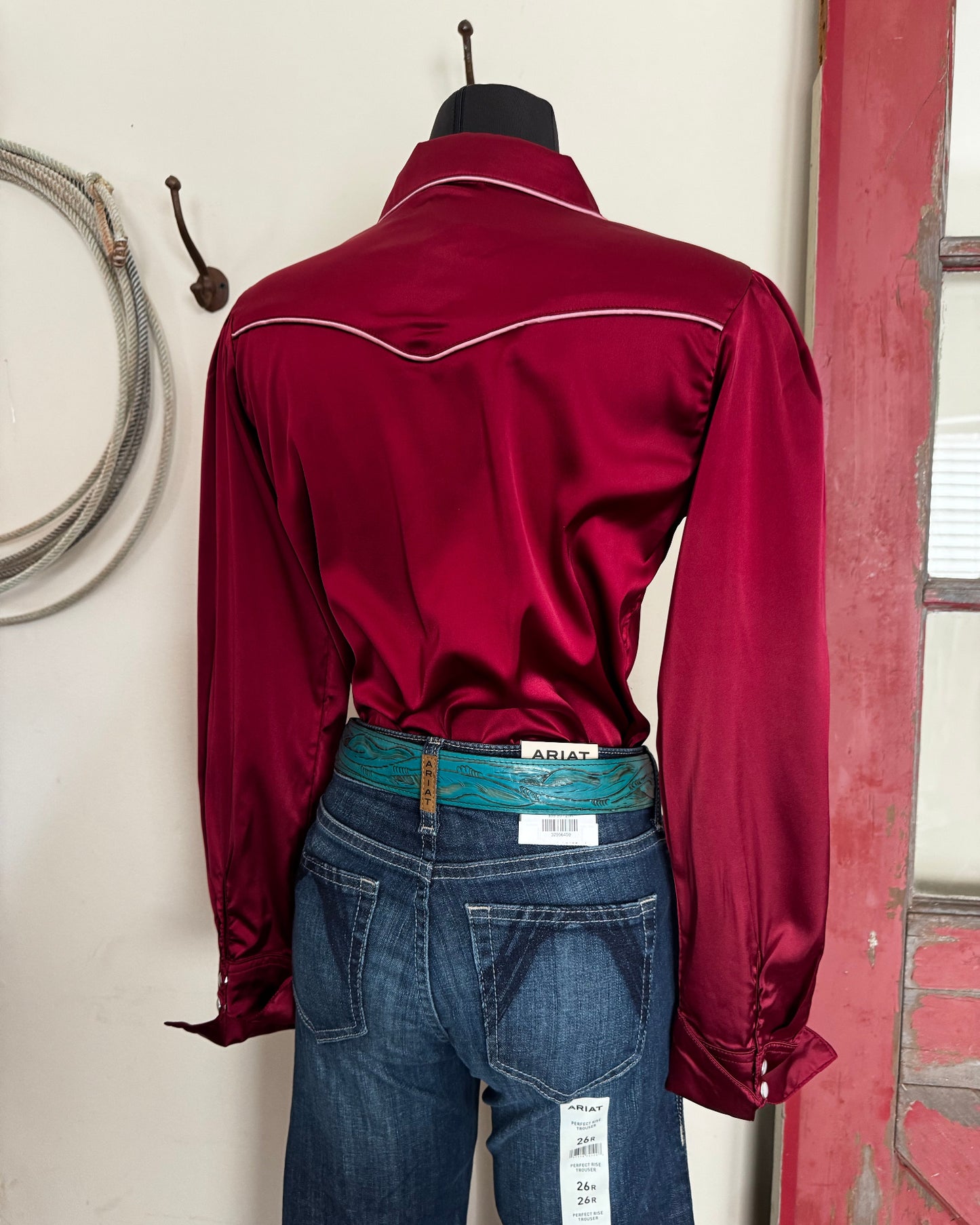 Maroon shirt and blue jeans on a white surface with a circular object in the background.