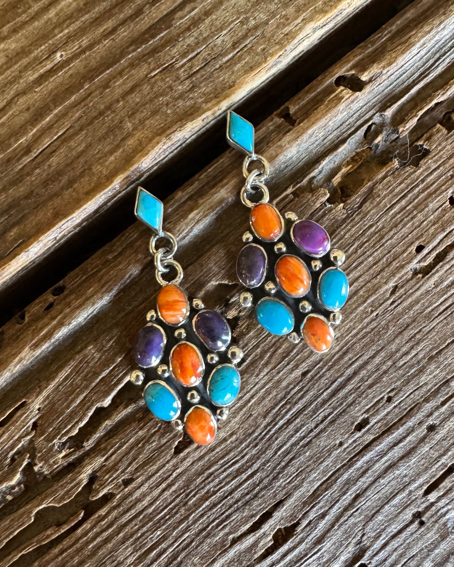 Sterling silver earrings with turquoise, orange and purple spiny stones on rustic wood background