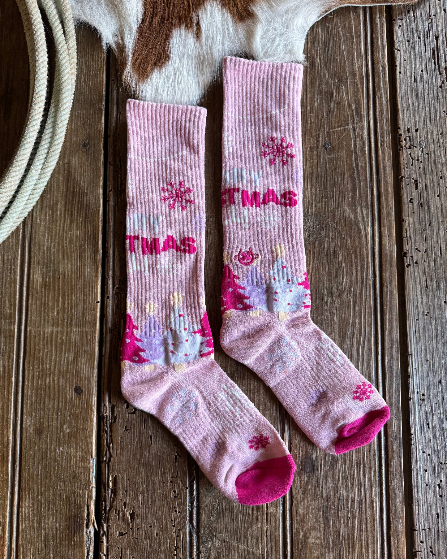 Pink Christmas-themed socks on a wooden surface with a cowhide rug underneath.