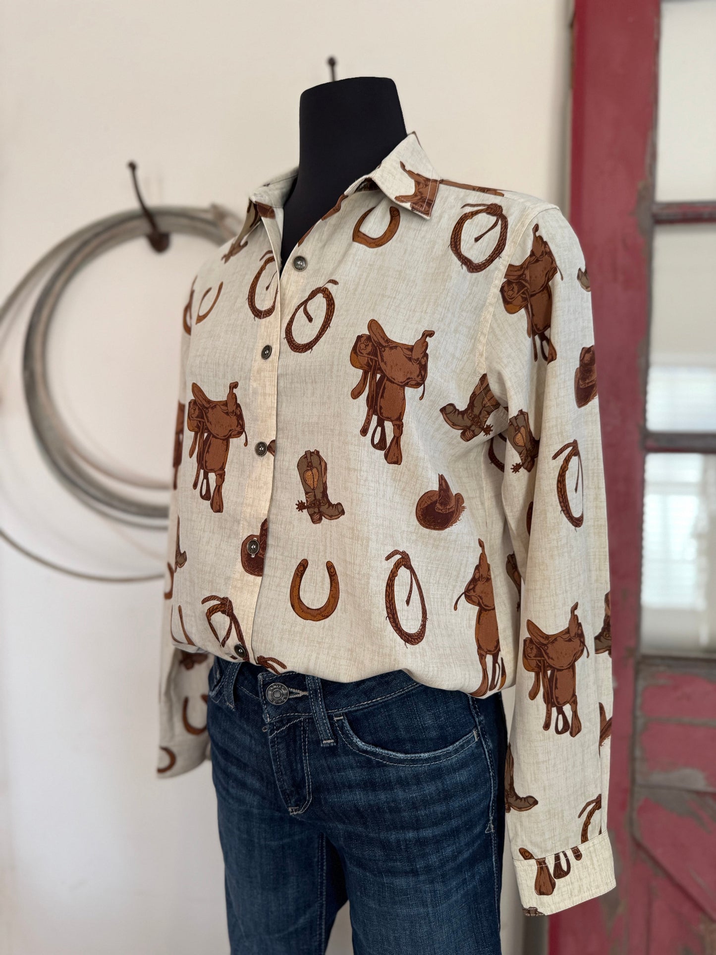 Mannequin wearing a patterned shirt with cowboy designs in a rustic setting.