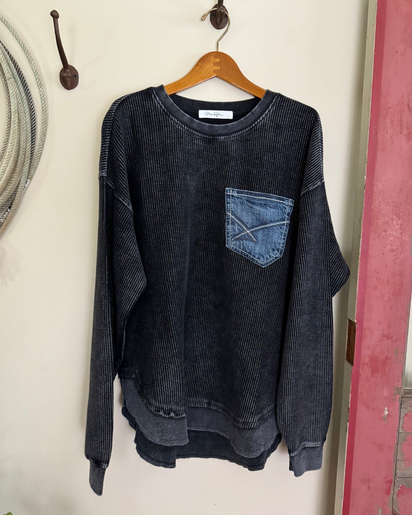 Folded black sweater with a patch on a wooden hanger against a white wall.