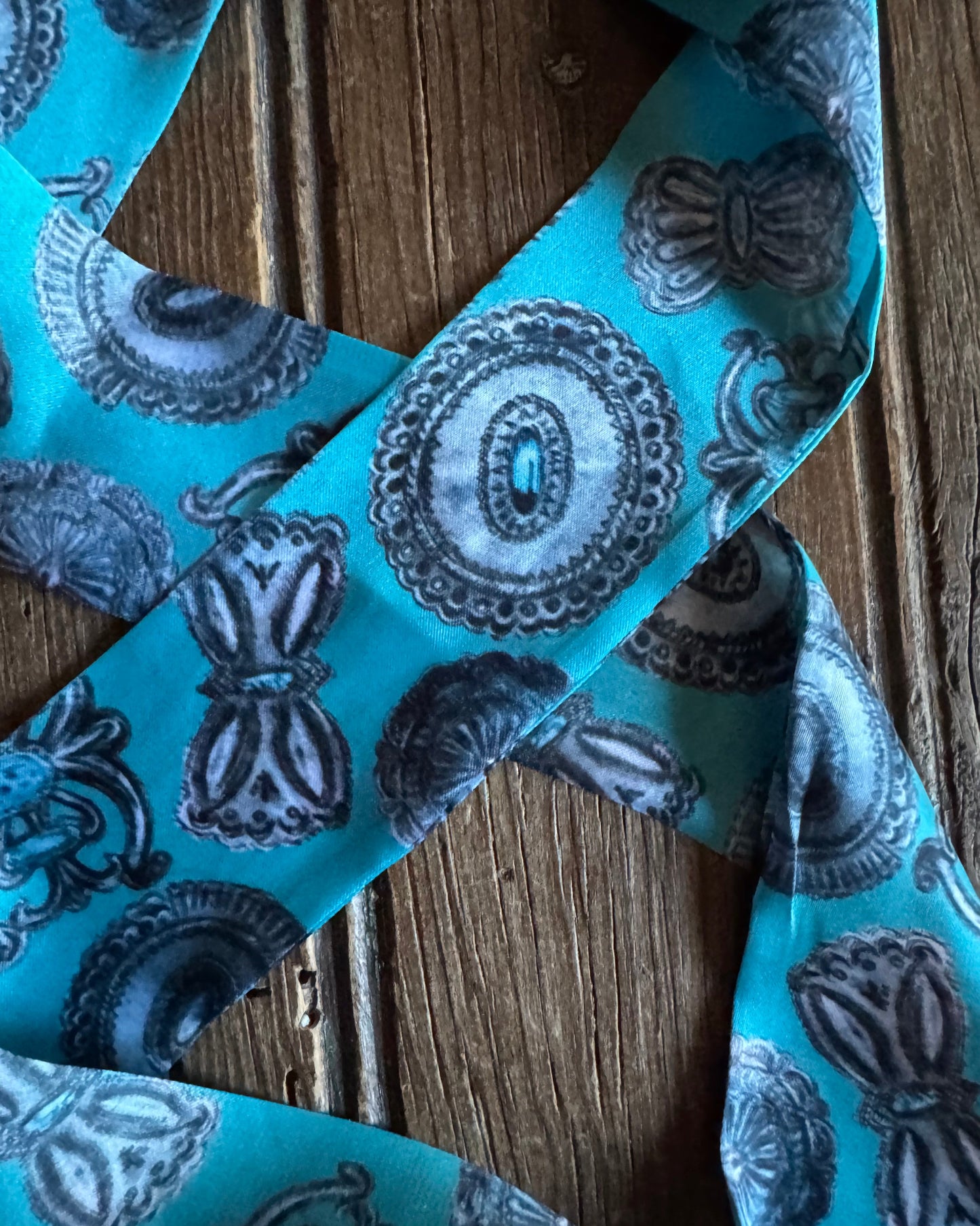 Turquoise ribbon scarf
with black decorative patterns on a wooden surface