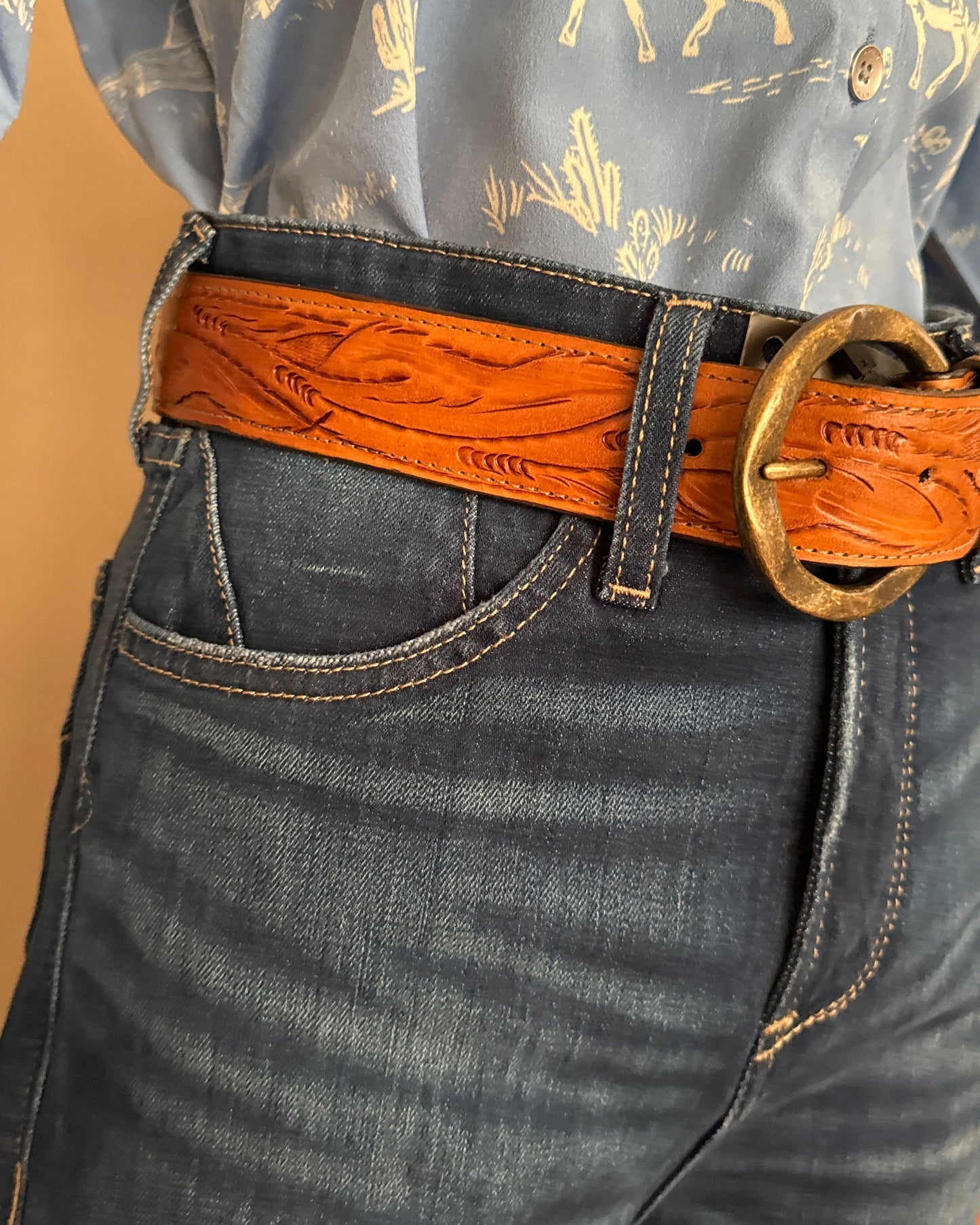 Close-up of a person wearing dark jeans with a brown leather belt.