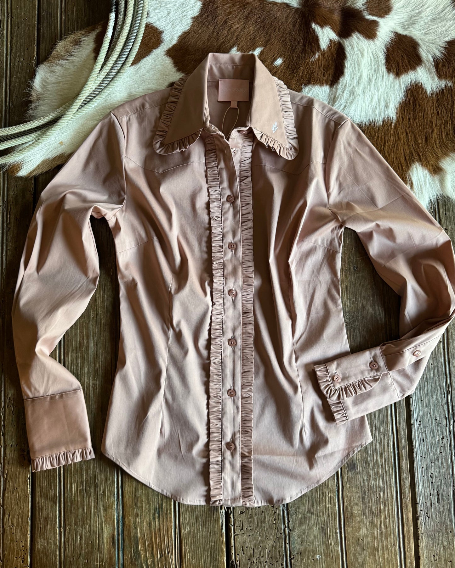 Pink blouse with ruffled details on a wooden surface with cowhide rug in the background
