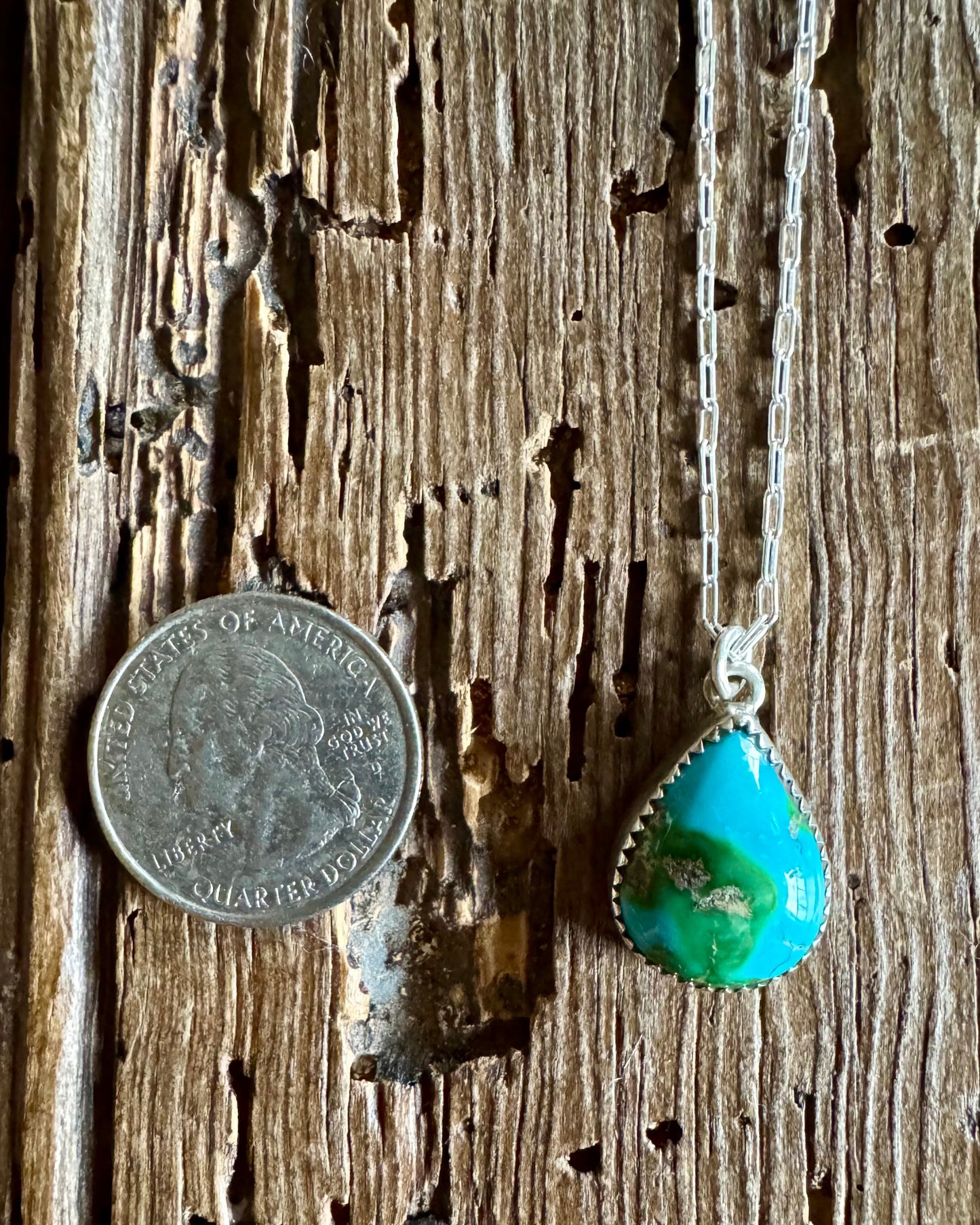Turquoise pendant necklace on a wooden surface with a coin for scale