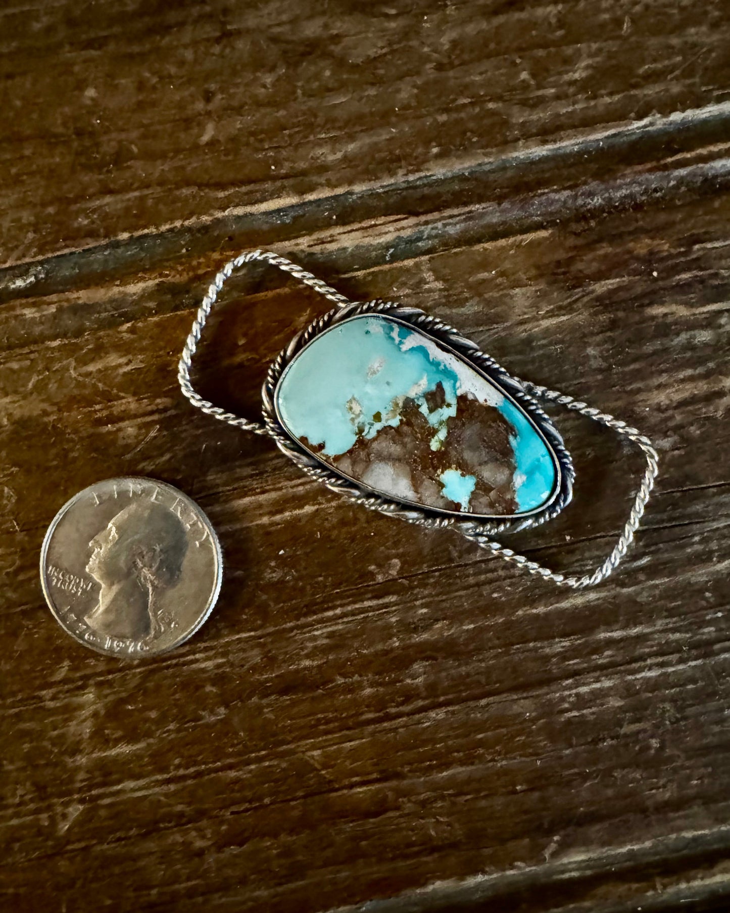 Turquoise stone pendant on a wooden surface with a quarter for scale