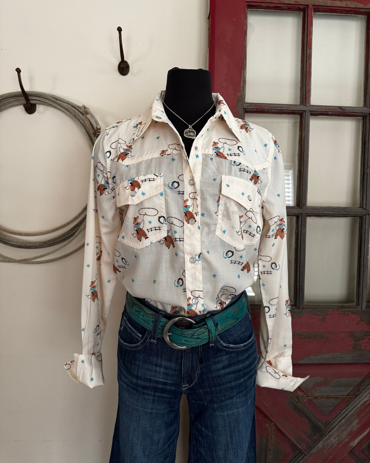 Mannequin wearing a patterned shirt and jeans standing in front of a window.