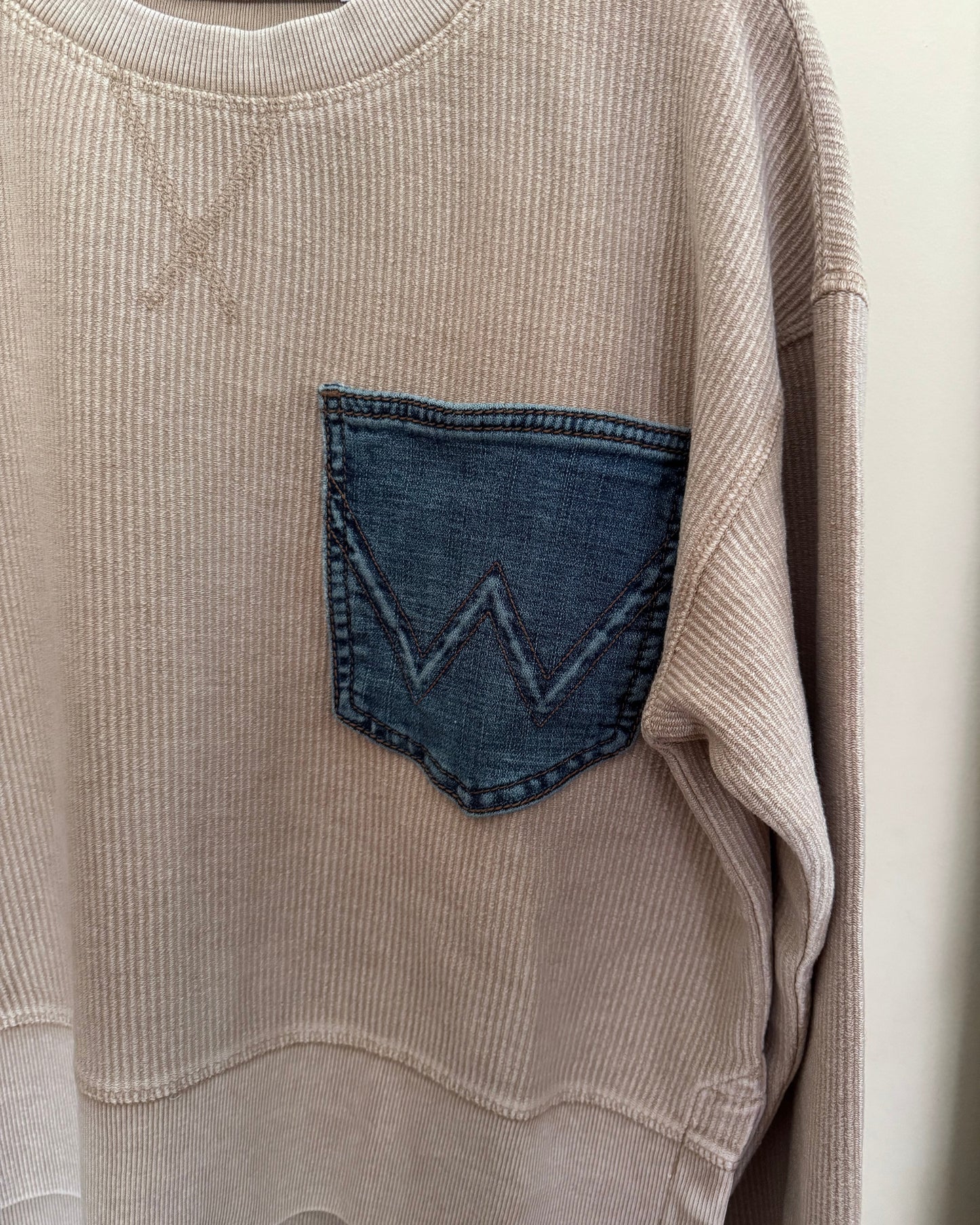 Close-up of a beige corduroy garment with a blue denim pocket detail.