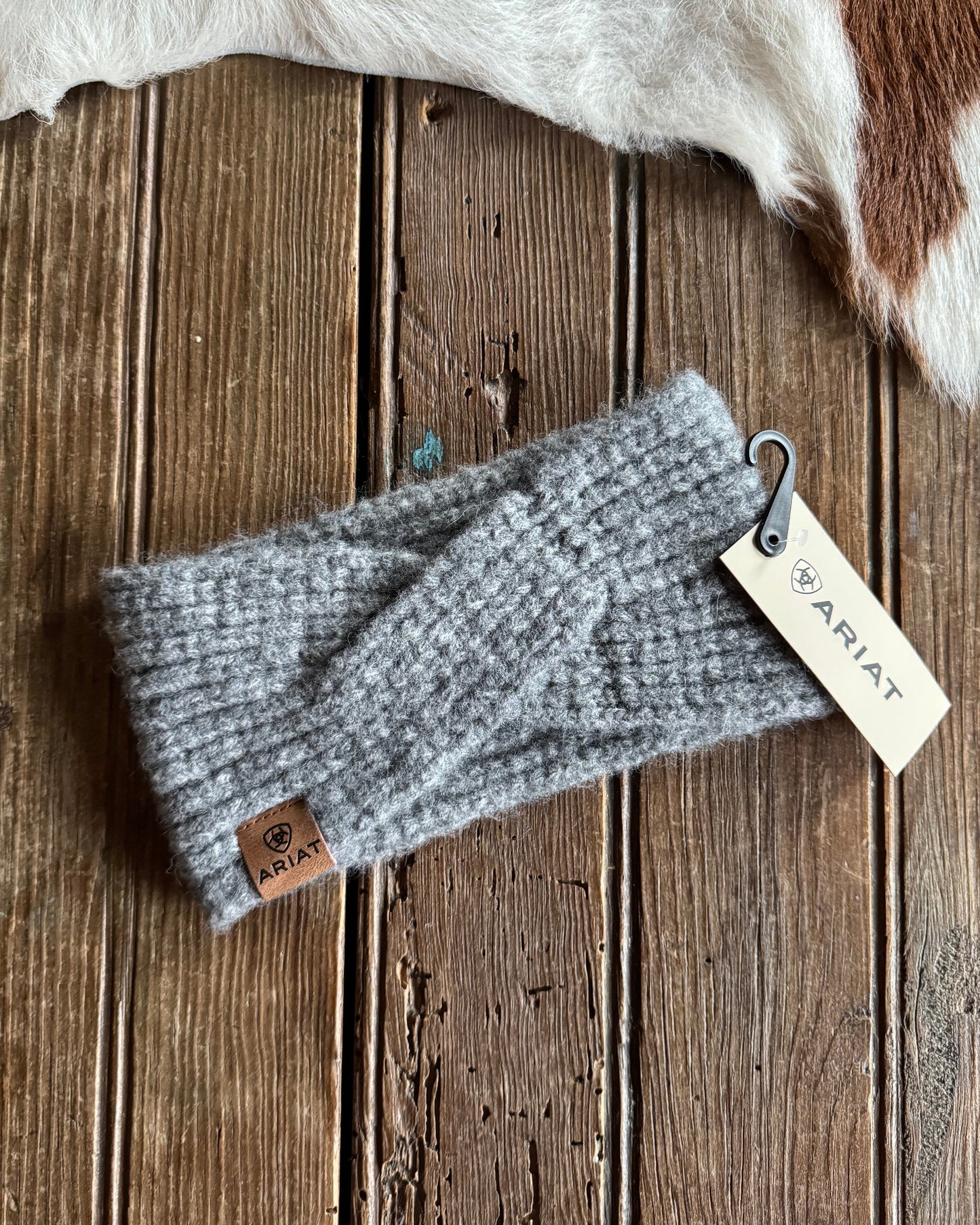 Gray knit headband with Ariat tag on a wooden surface
