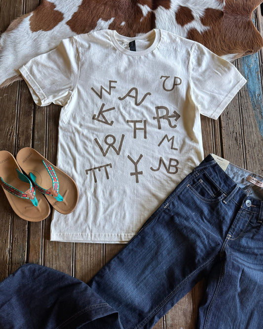 White t-shirt with brown text, blue jeans, and sandals on a wooden surface.