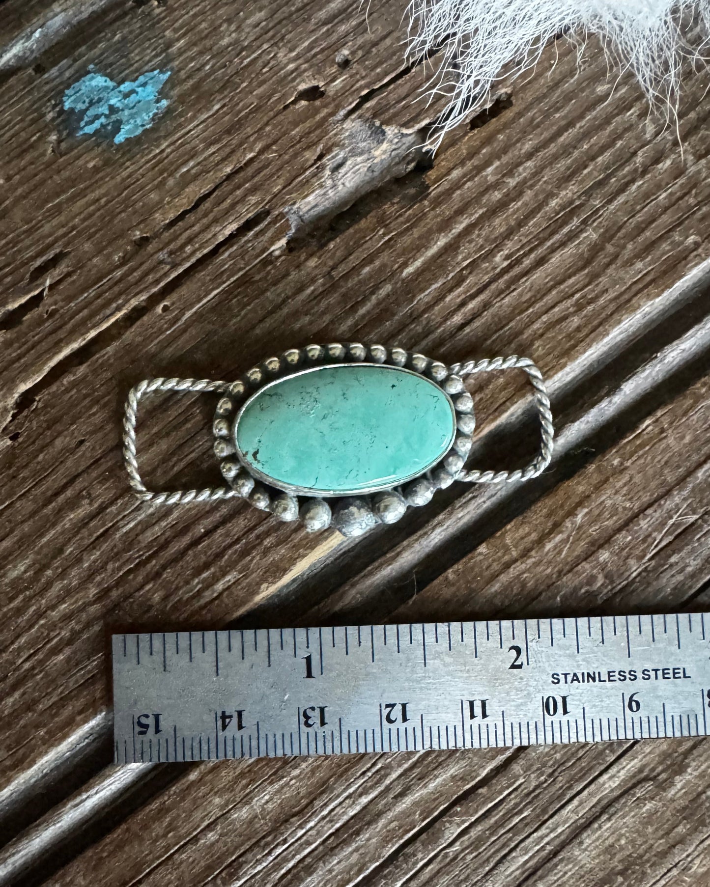 Turquoise stone pendant with silver chain on a wooden surface with a ruler for scale.