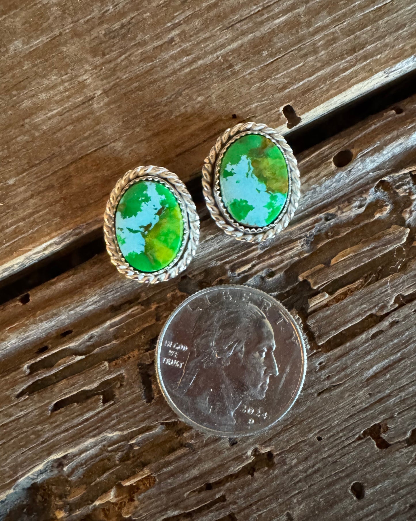 Pair of earrings with green stones next to a penny on wooden surface