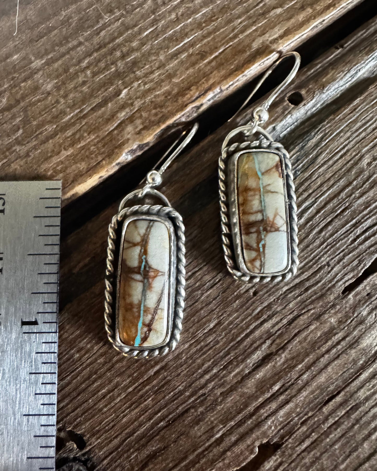 Pair of earrings with stone inlays on a wooden surface with a ruler for scale.