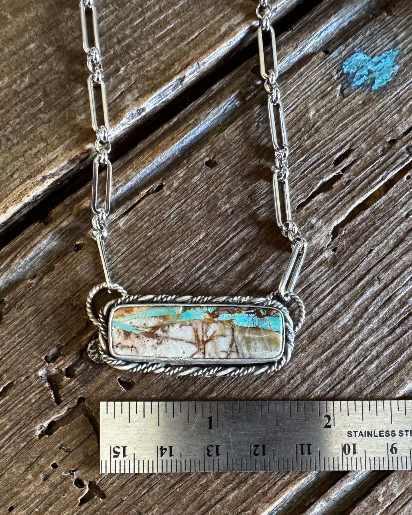 Necklace with a pendant next to a ruler on a wooden surface
