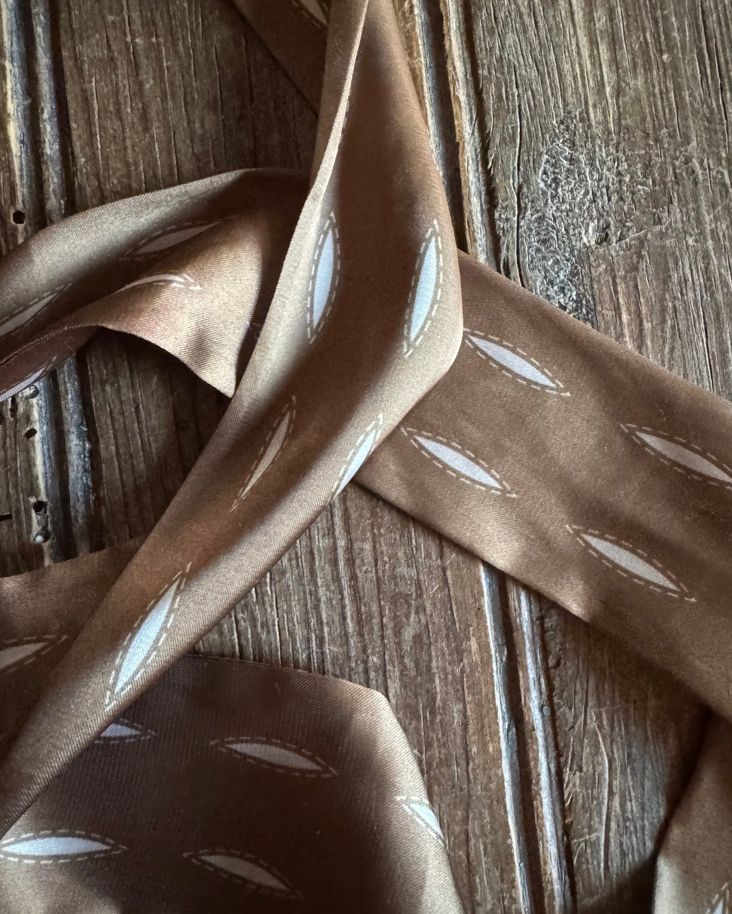 Brown ribbon scarf with white leaf patterns on a wooden surface