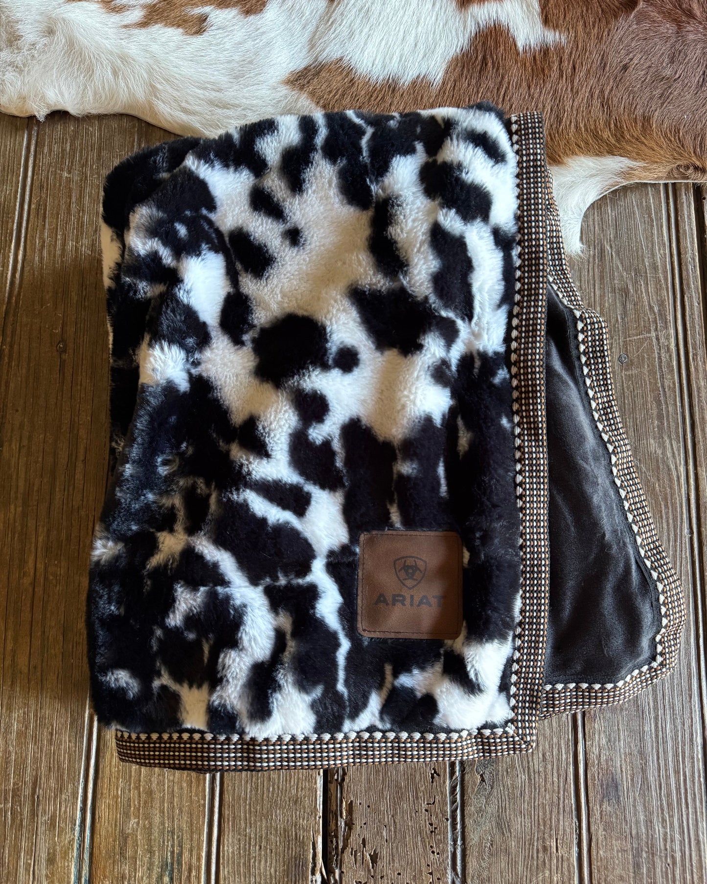cow print blanket with ribbon trim on a wooden surface