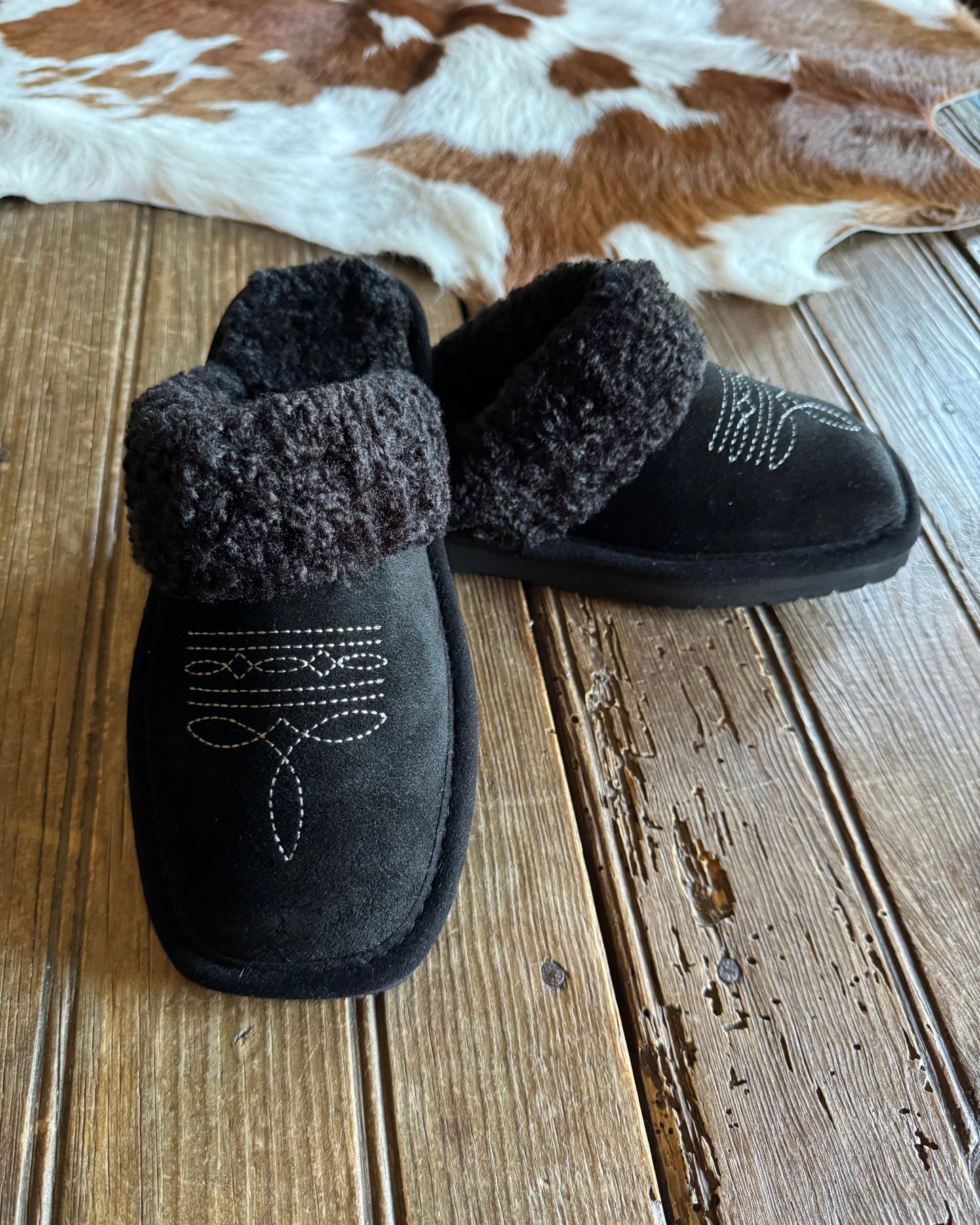 Black slippers with fuzzy texture on a wooden floor